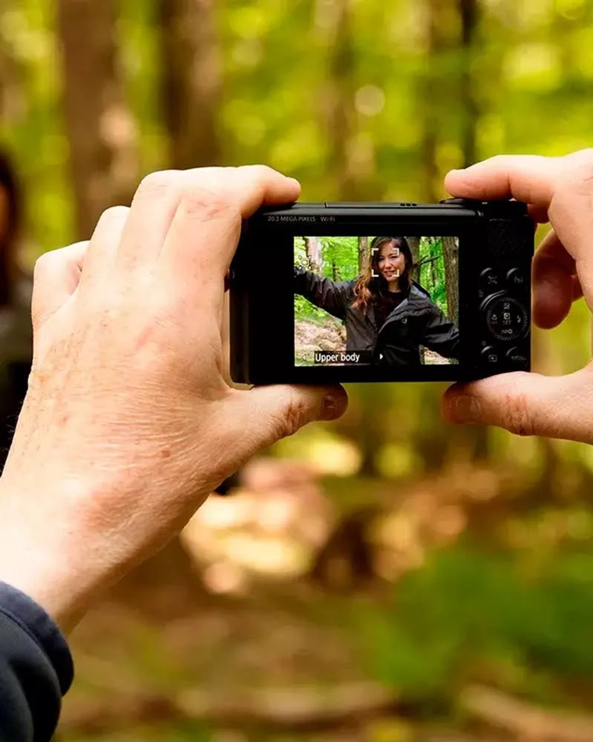 Osoba trzyma aparat, robiąc zdjęcie kobiecie w lesie. Ekran pokazuje twarz kobiety.