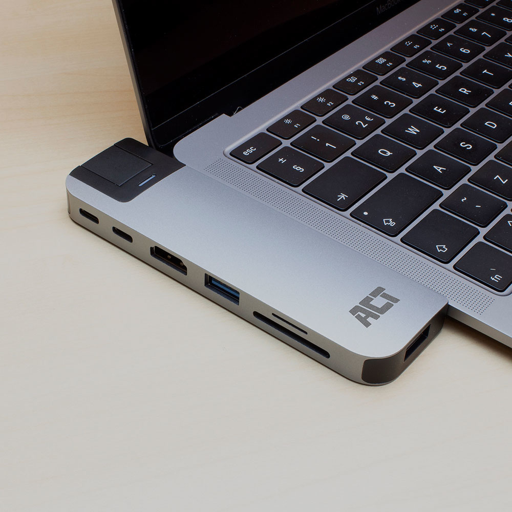 Ein silbernes Laptop mit angeschlossenem Hub, der Anschlüsse und den Markennamen 'ACT' zeigt, auf Holzoberfläche.