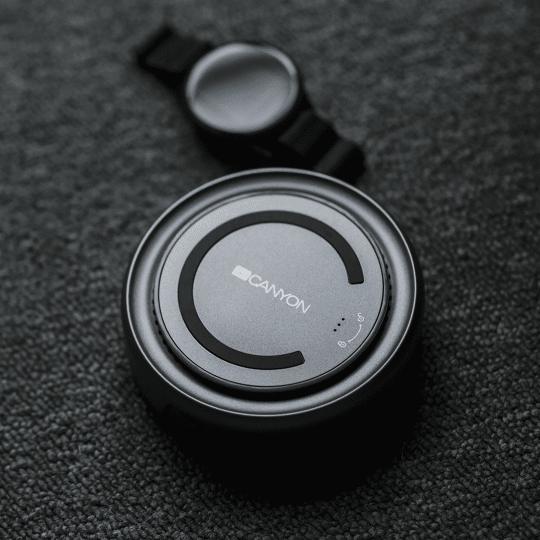 Srebrna ładowarka bezprzewodowa Canyon i smartwatch Canyon na ciemnoszarej powierzchni, widok z góry.