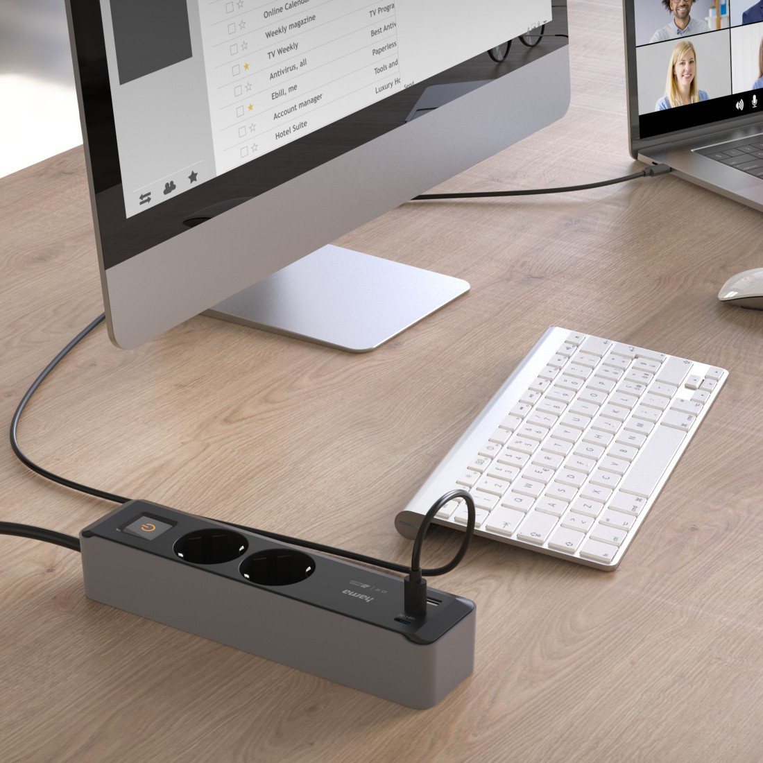 Konfiguracja komputera z monitorem, klawiaturą i listwą zasilającą na drewnianym stole.