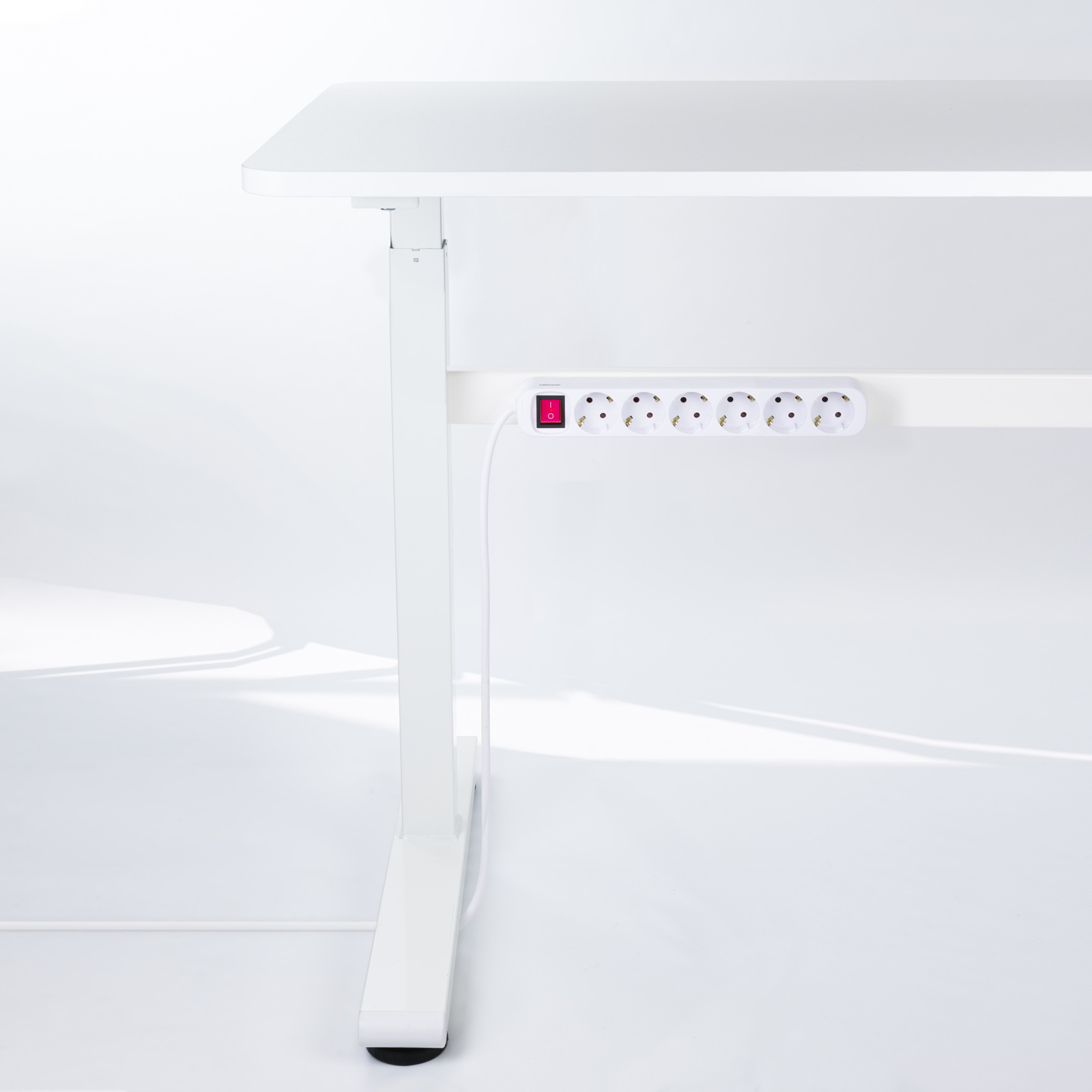 Białe biurko z listwą zasilającą i czerwonym włącznikiem pod spodem. Białe tło.