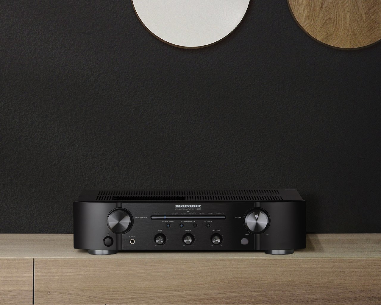 Schwarzer Marantz-Stereo-Receiver auf Holz, dunkler Wandhintergrund mit zwei runden Dekorelementen.