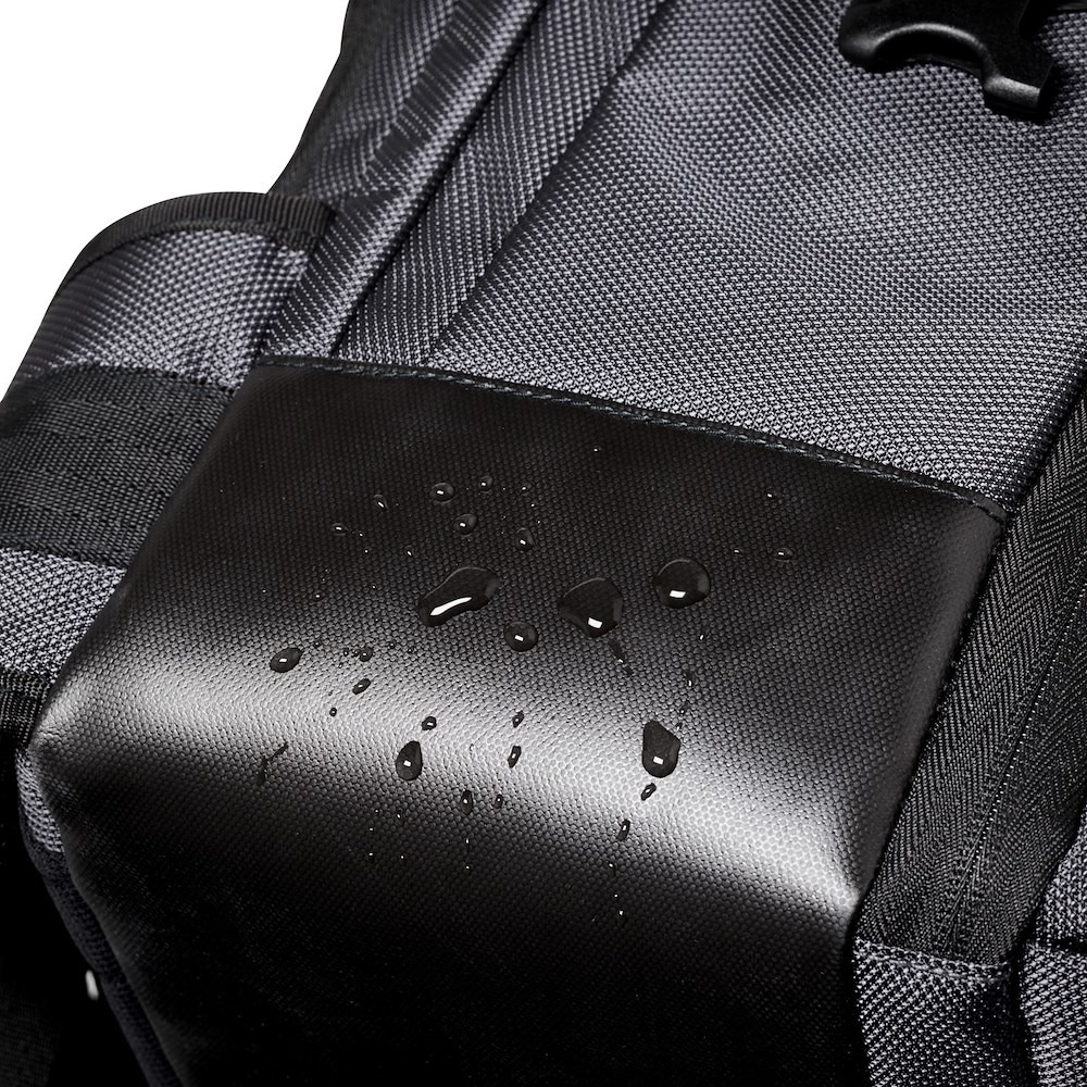Schwarzes Rucksackdetail. Nahaufnahme einer schwarzen, strukturierten Tasche mit Wassertropfen darauf.