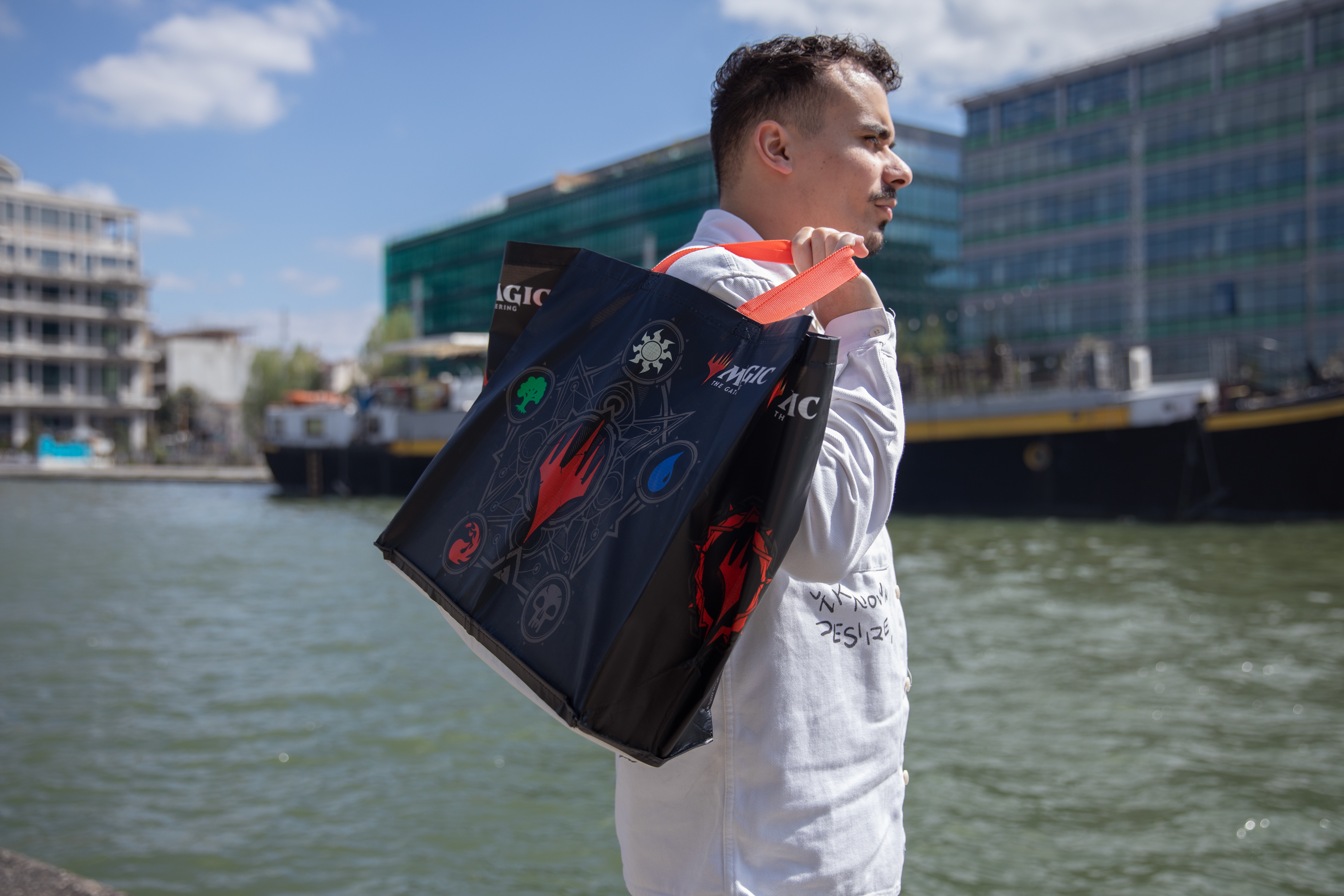 Una persona con una bata blanca lleva una bolsa negra con el logo de Magic the Gathering.