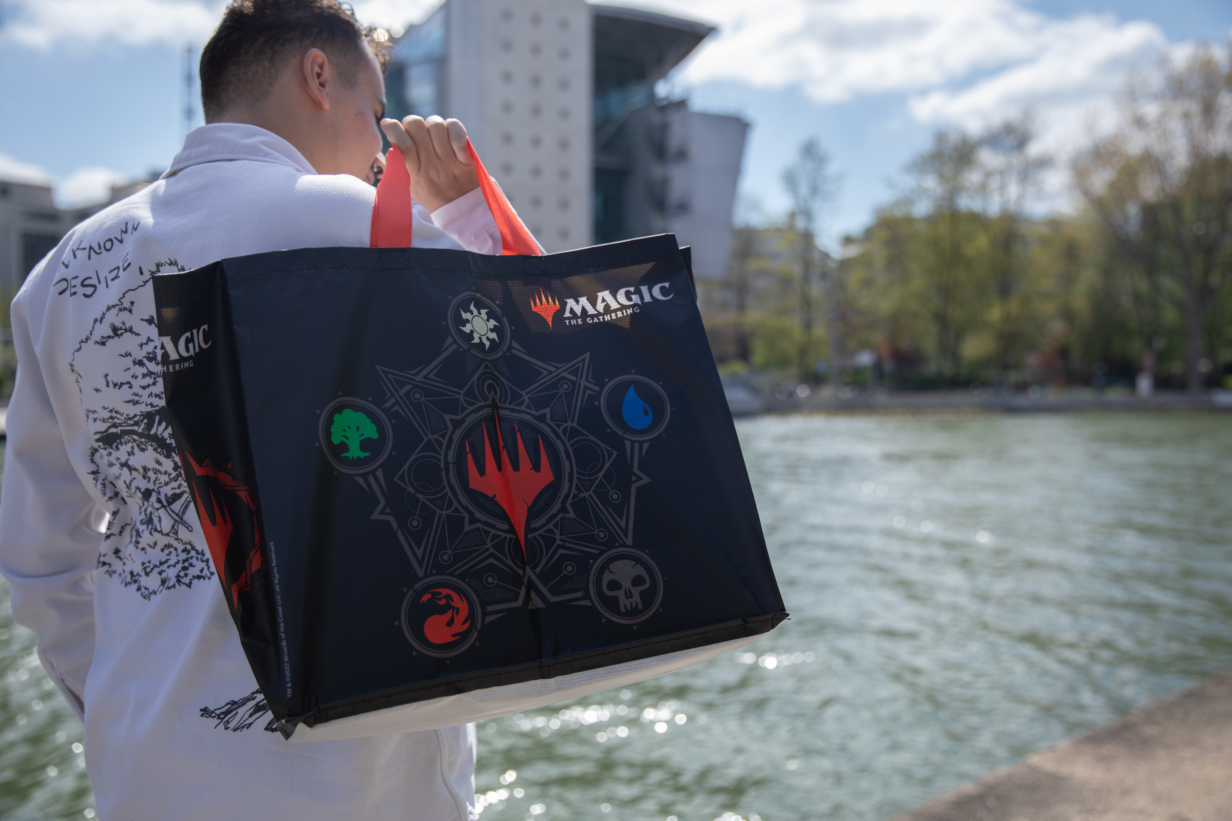 Persona sosteniendo una bolsa negra de Magic: The Gathering junto al agua.