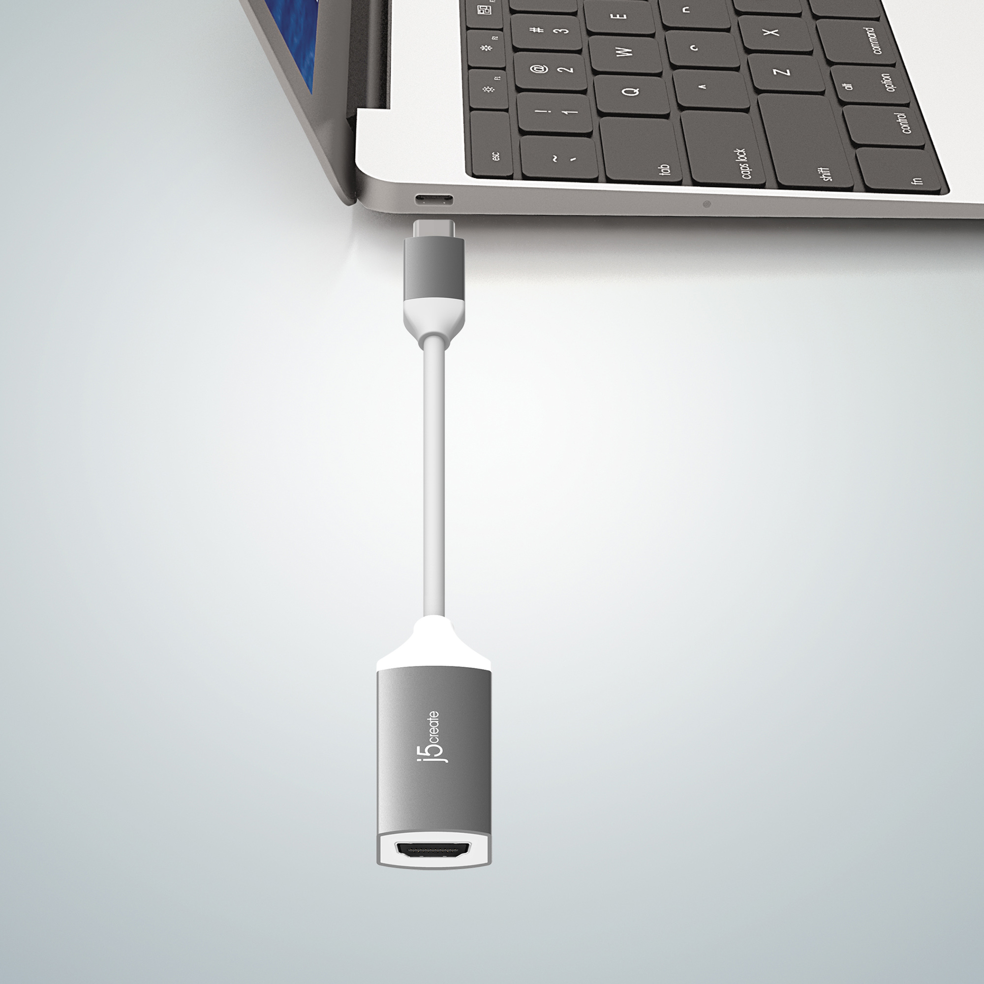 Un adaptador USB-C a HDMI gris conectado a una computadora portátil. El adaptador tiene un logotipo blanco.