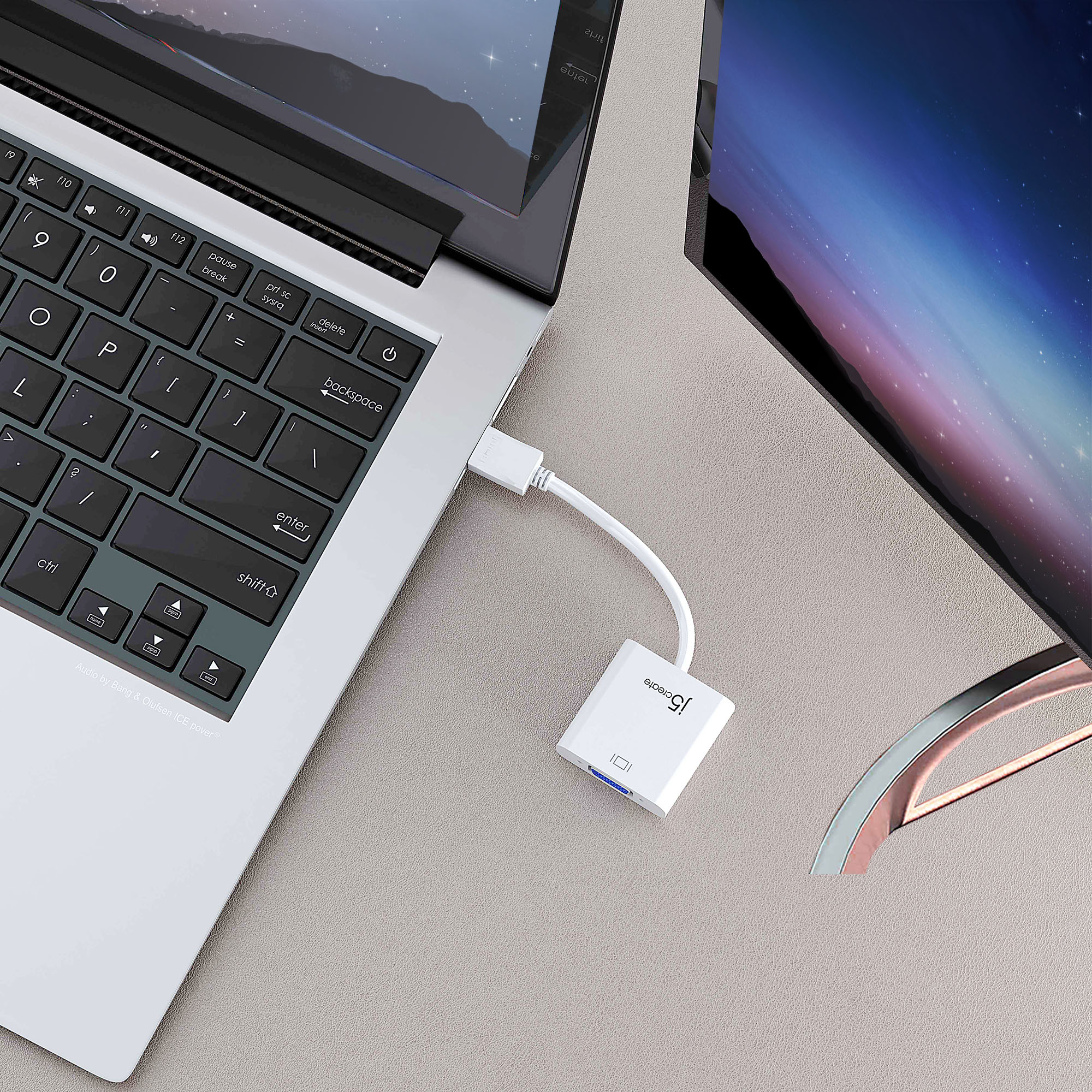 Laptop conectado a un monitor mediante un adaptador blanco. Ambos dispositivos están sobre una superficie gris.