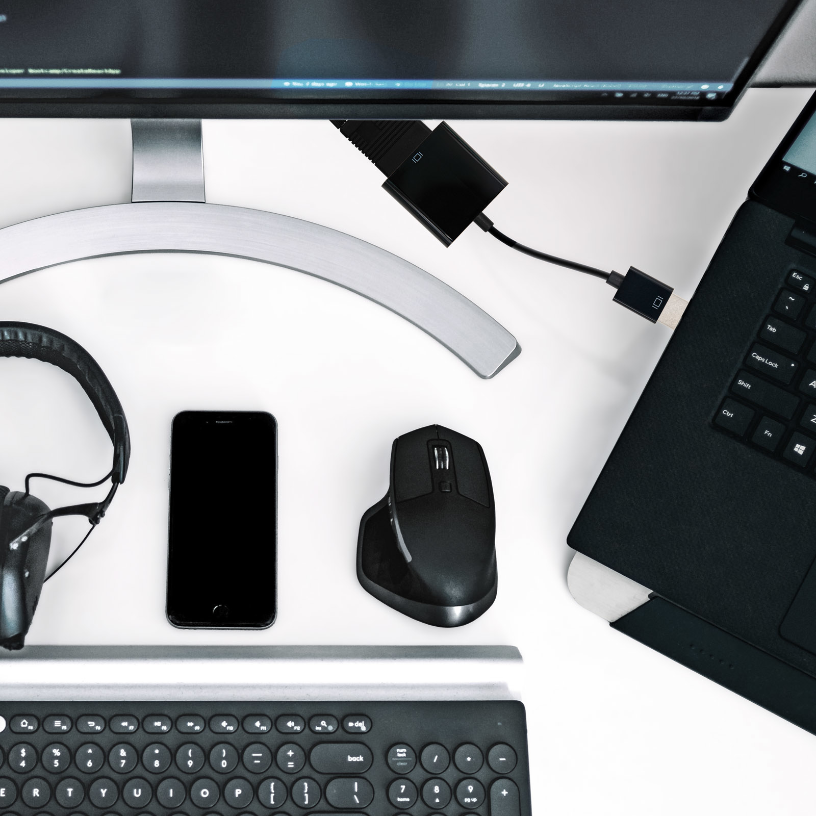 Configuración de escritorio con monitor, teléfono, teclado, ratón, auriculares y cable negro.