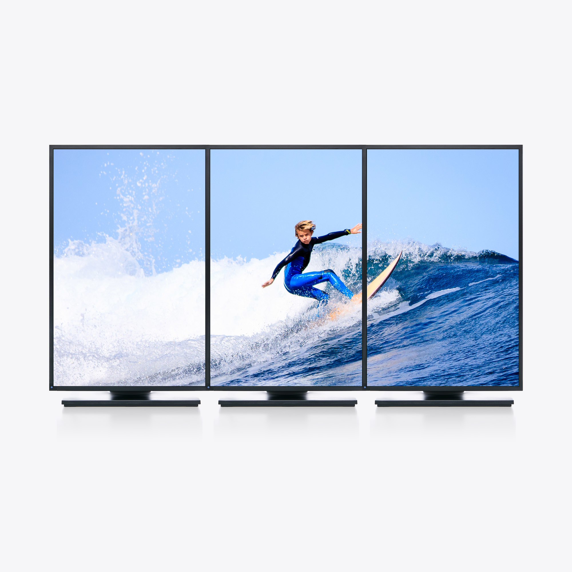 Drei nebeneinander stehende Fernseher zeigen einen Surfer auf einer Welle. Blauer Himmel im Hintergrund.