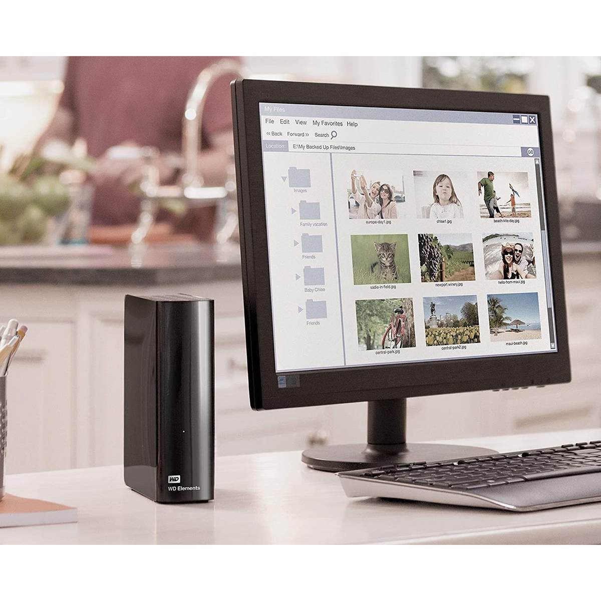 Czarny zewnętrzny dysk twardy obok komputera pokazującego foldery plików i obrazy.