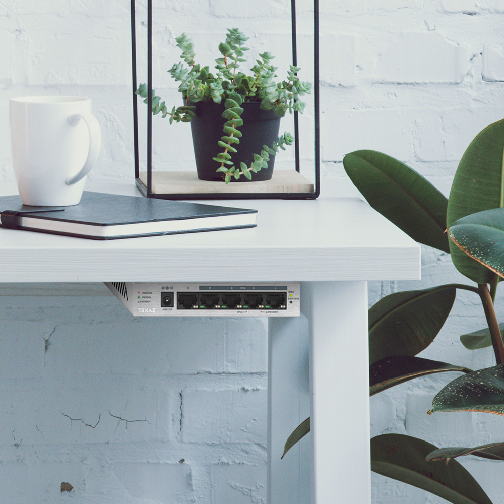 Białe biurko z routerem. Widoczna roślina, kubek i notatnik. Biała ceglana ściana.