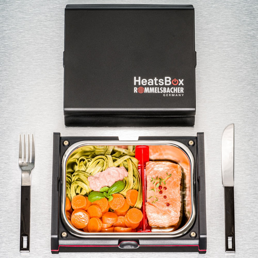 HeatsBox-Behälter mit Essen: Lachs, Nudeln, Karotten. Gabel und Messer daneben.