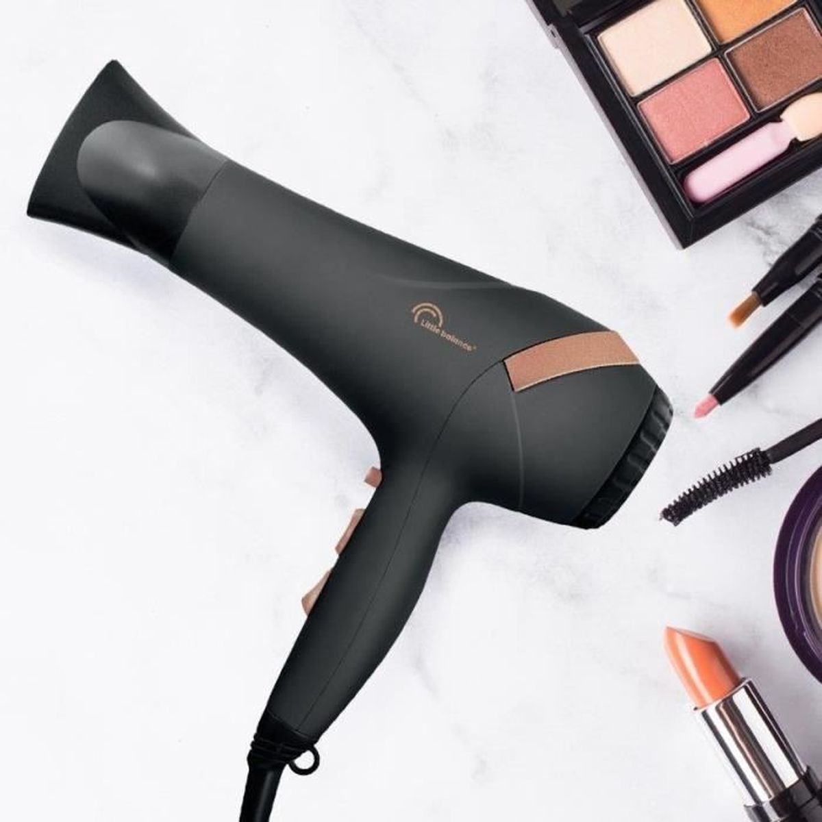 Czarna suszarka do włosów z kosmetykami. Suszarka ma uchwyt i złoty detal.