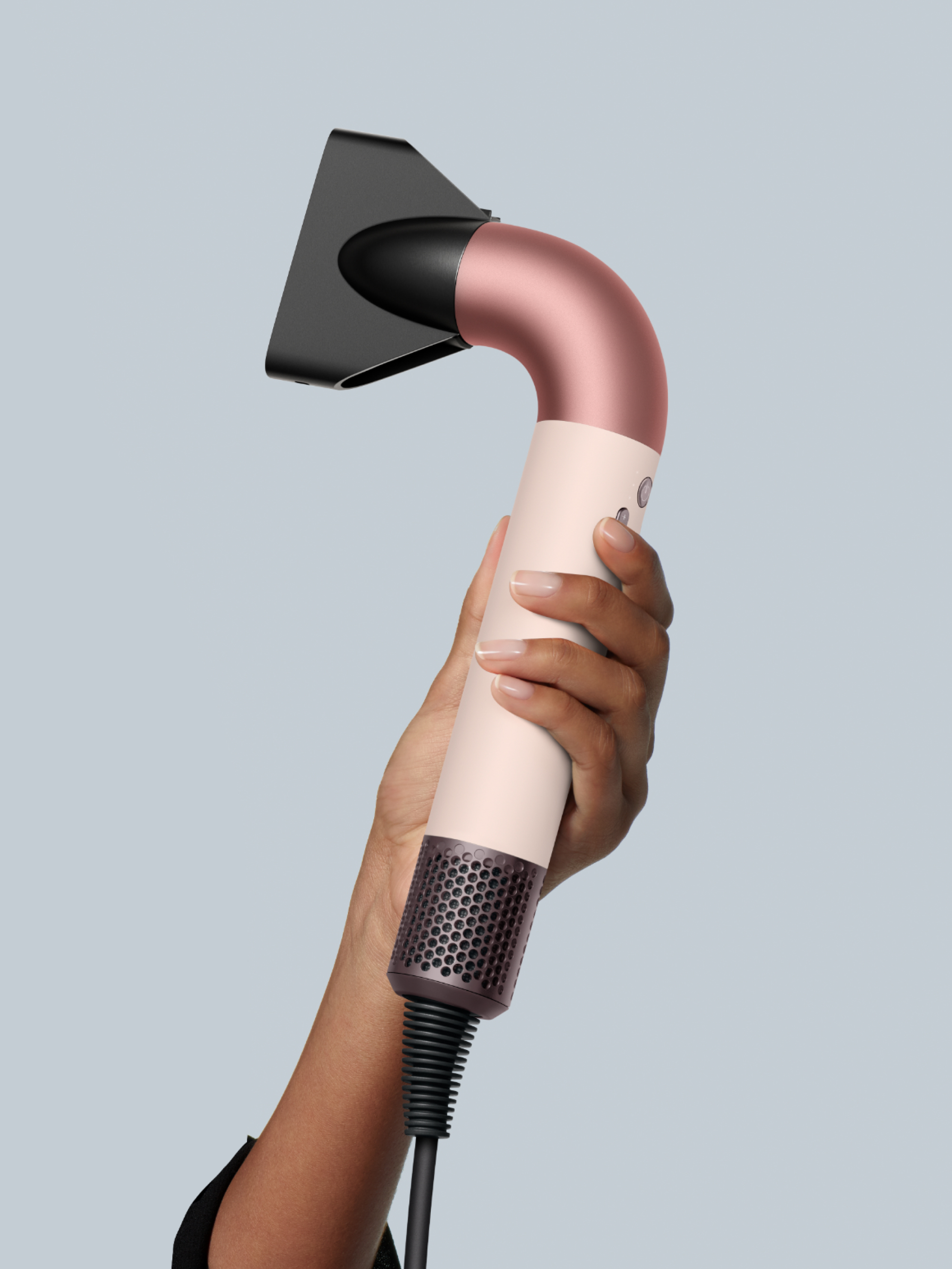 Una persona tiene in mano un asciugacapelli color oro rosa e crema con un beccuccio nero.