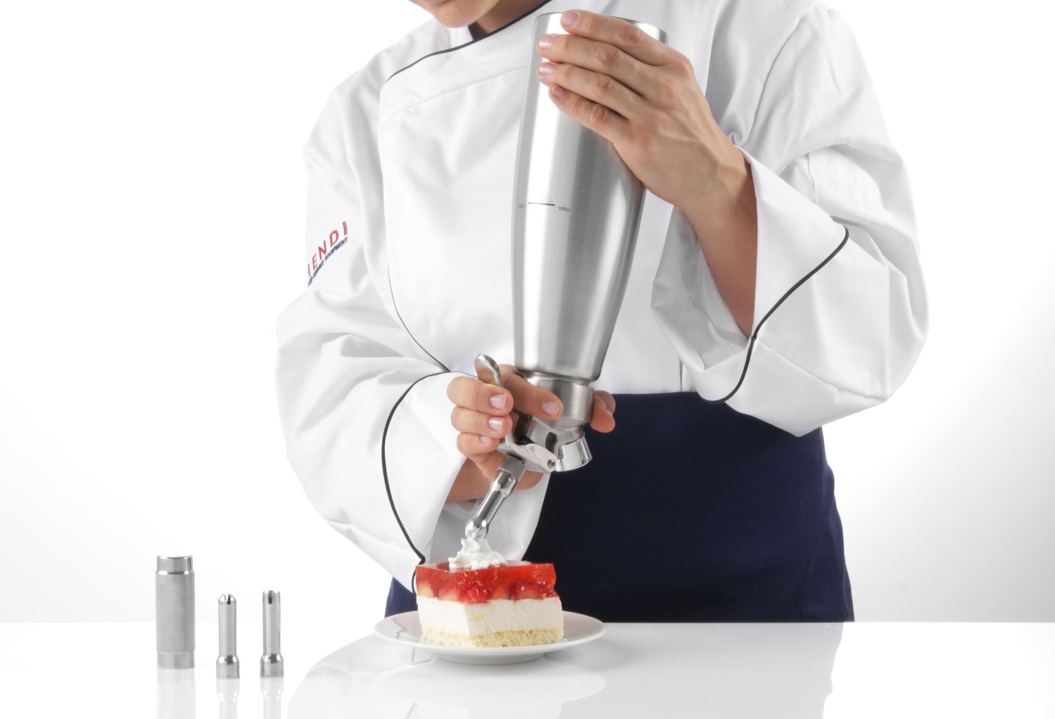 Koch in weißer Uniform verwendet einen Spender, um einen Kuchen mit Schlagsahne zu belegen.