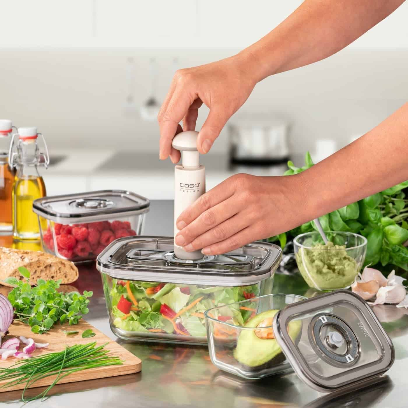 Persona che utilizza una macchina per sottovuoto su un contenitore di vetro con verdure.