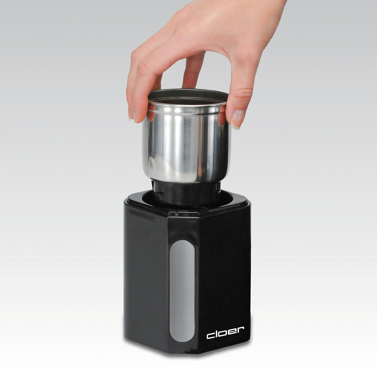 Eine Hand, die einen silbernen Behälter in eine schwarze Basis einsetzt, Teil einer Kaffeemühle.