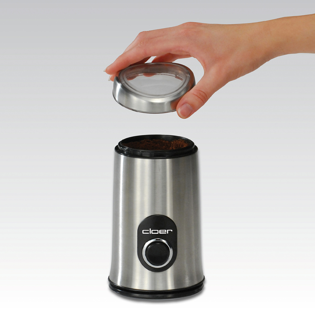 Eine Kaffeemühle aus Edelstahl, mit einer Hand, die den Deckel abnimmt.