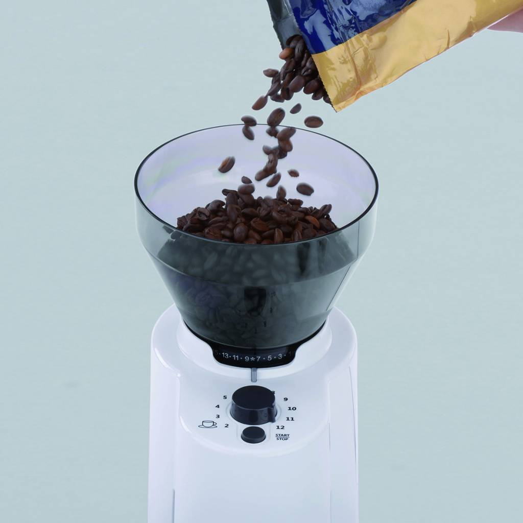 Kaffeebohnen, die in einen transparenten Behälter in einer weißen Kaffeemühle gegossen werden.