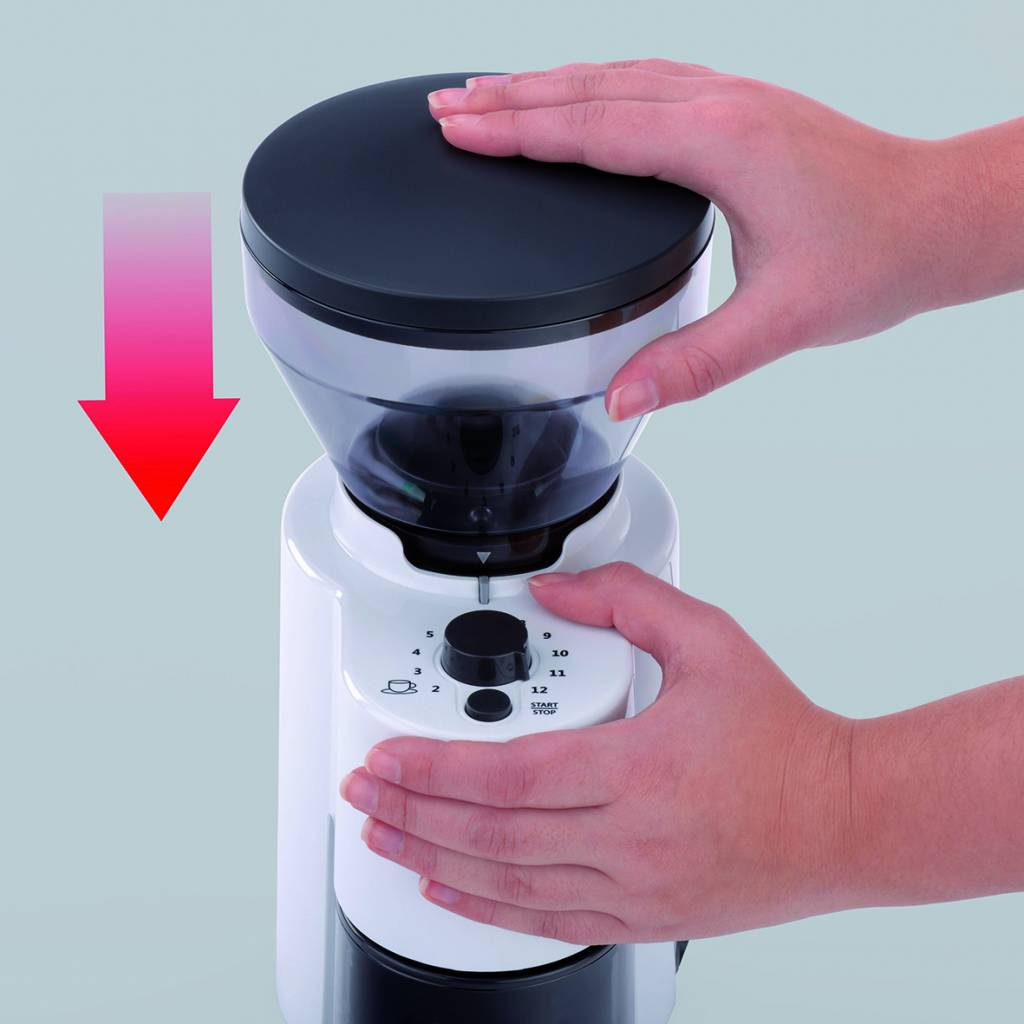 Hände bedienen eine weiß-schwarze Kaffeemühle. Roter Pfeil zeigt auf die Mühle.