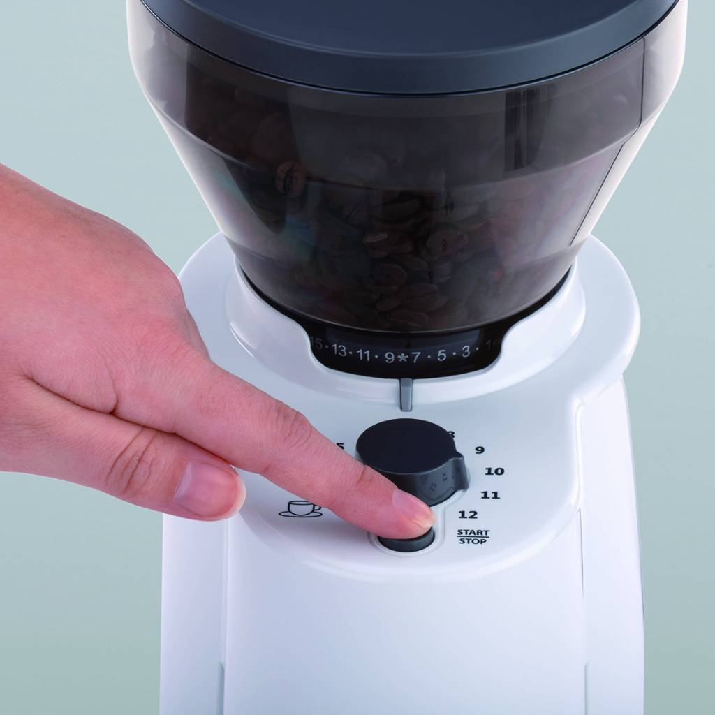 Die Hand einer Person drückt eine Taste an einer weißen Kaffeemühle mit Kaffeebohnen.