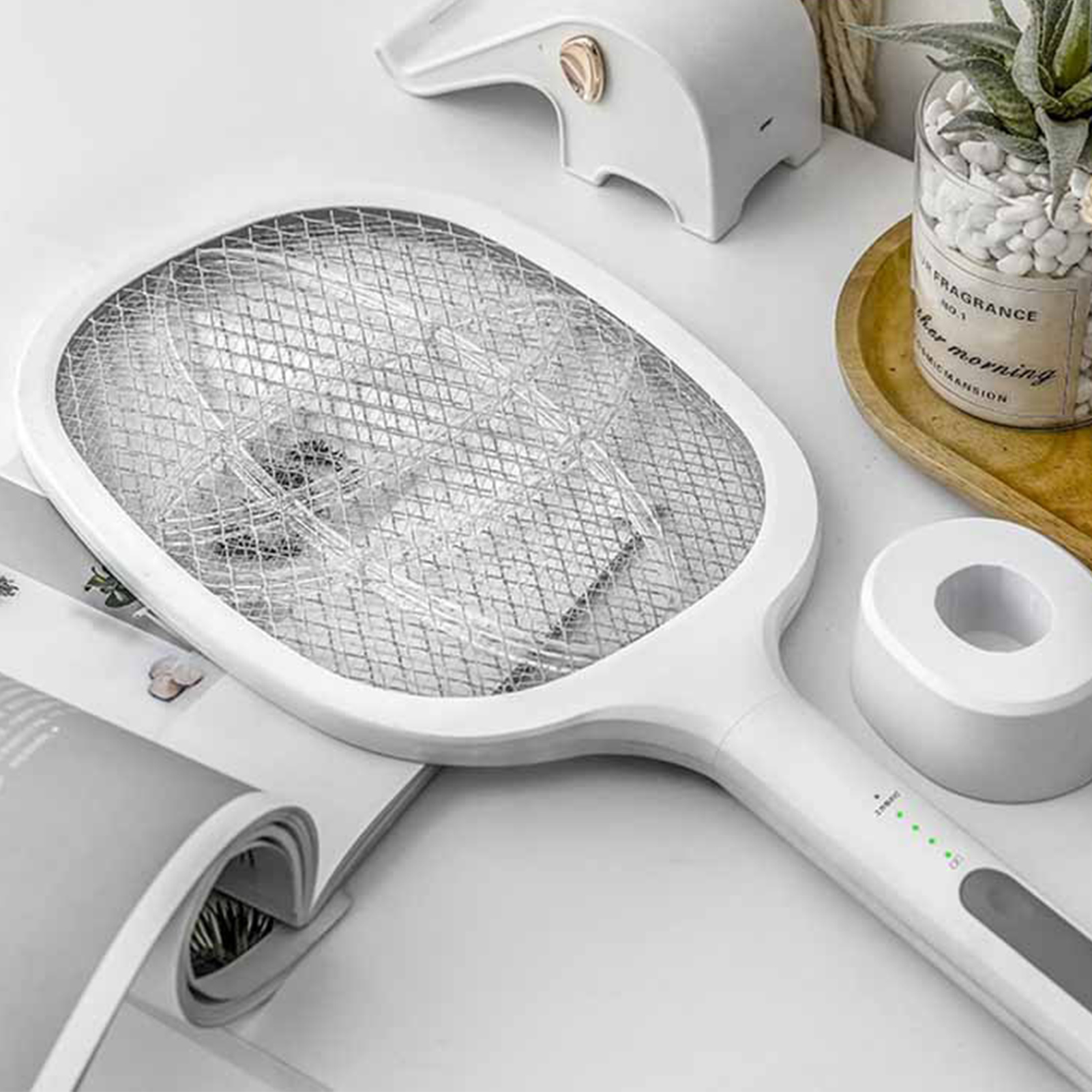 Weißer elektrischer Fliegenfänger mit Gitter, Griff und grünen Stromanzeigen auf einem Tisch.