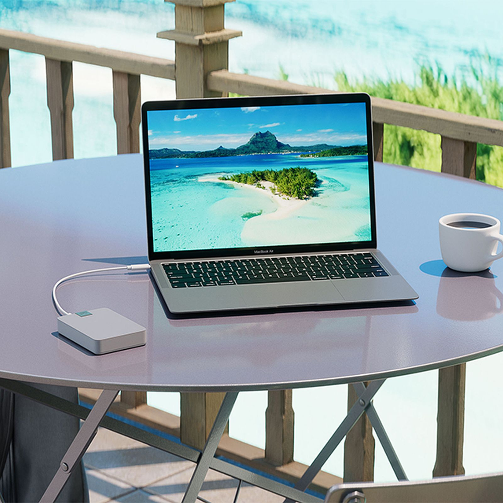 Laptop na stole, z piękną scenerią plażową na ekranie, białym kubkiem i stacją ładującą.