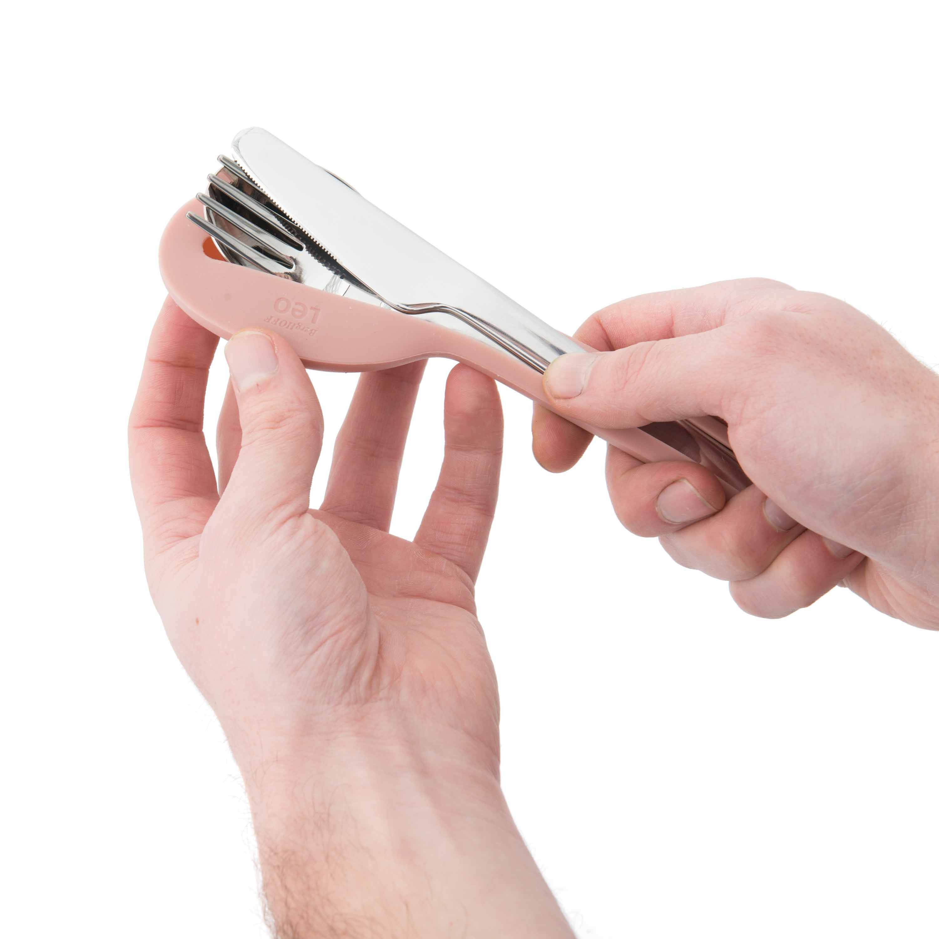 Mani che tengono un set di posate da viaggio rosa e argento con forchetta e coltello, sfondo bianco.