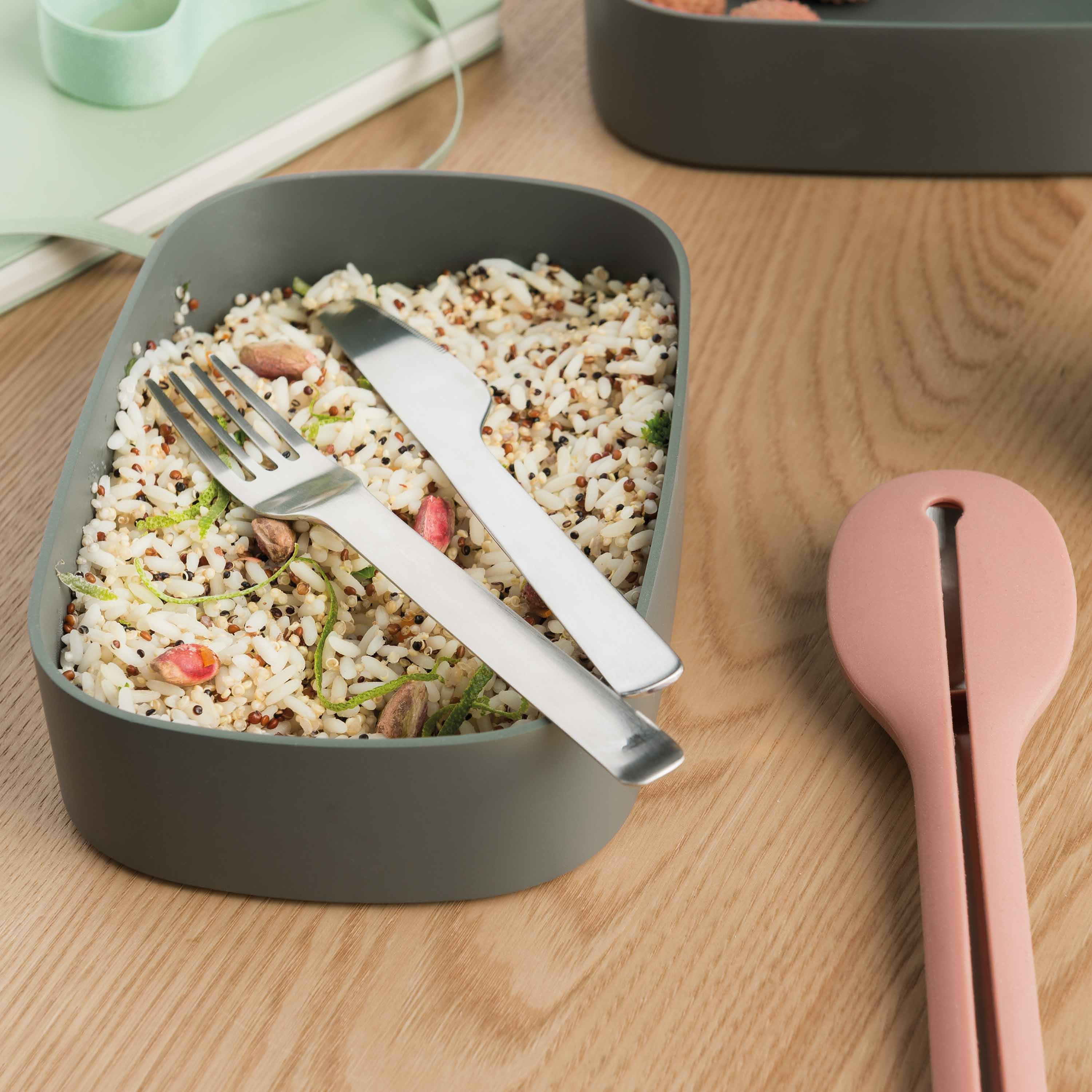 Scatola per il pranzo con cereali, una forchetta, un coltello e un cucchiaio, su una superficie di legno.
