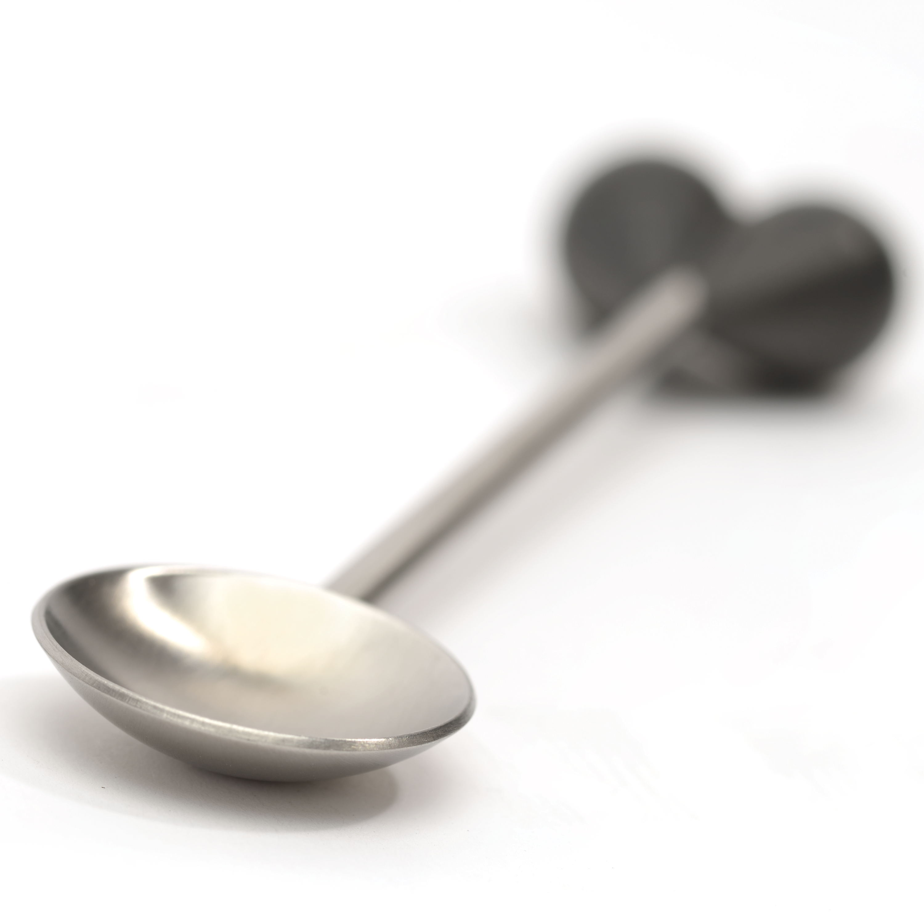 Silver spoon on white. Spoon bowl is in focus. The handle heart shape is blurred.