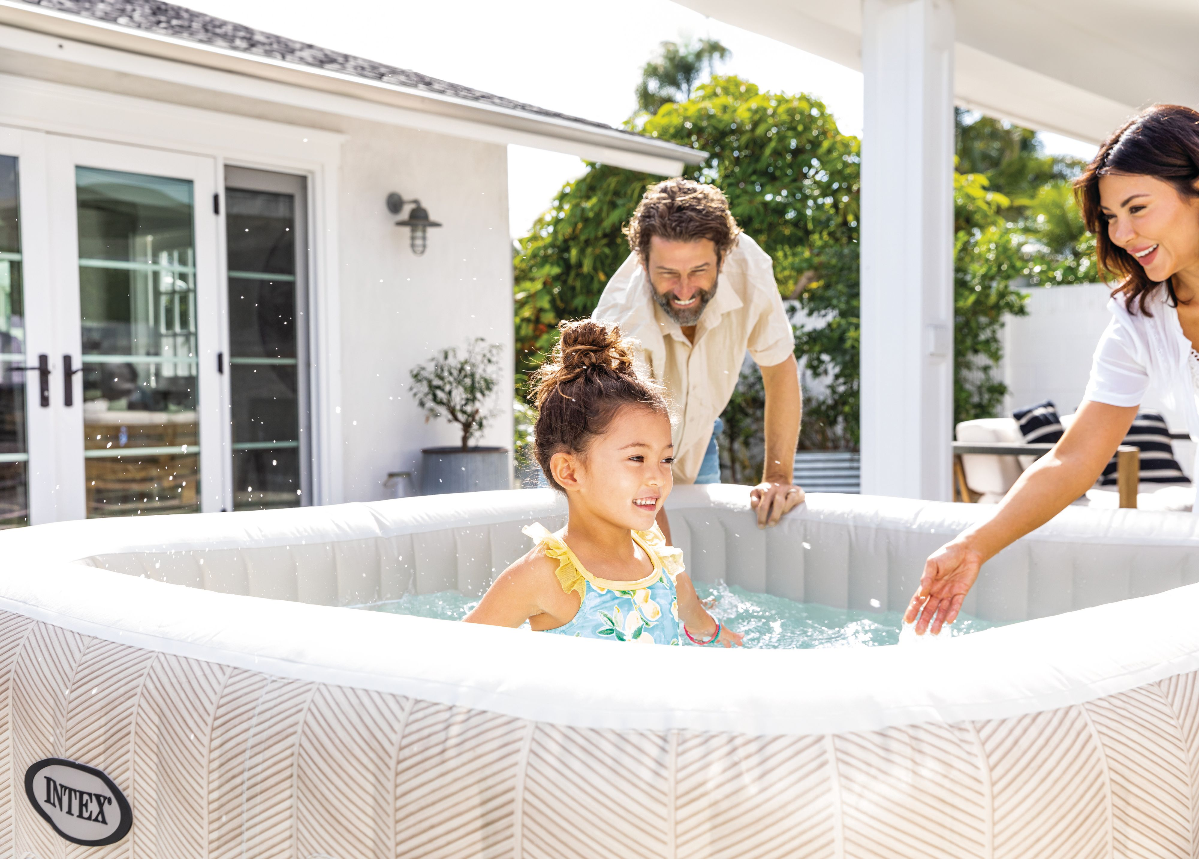 Rodzina w jacuzzi na podwórku. Dziewczynka w basenie, rodzice obserwują, słoneczny dzień.
