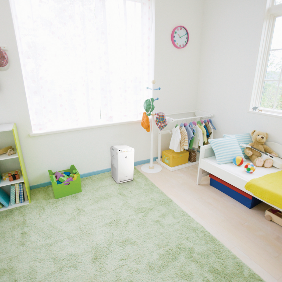 Chambre d'enfant avec tapis vert, purificateur d'air, étagère à jouets, lit et fenêtre.