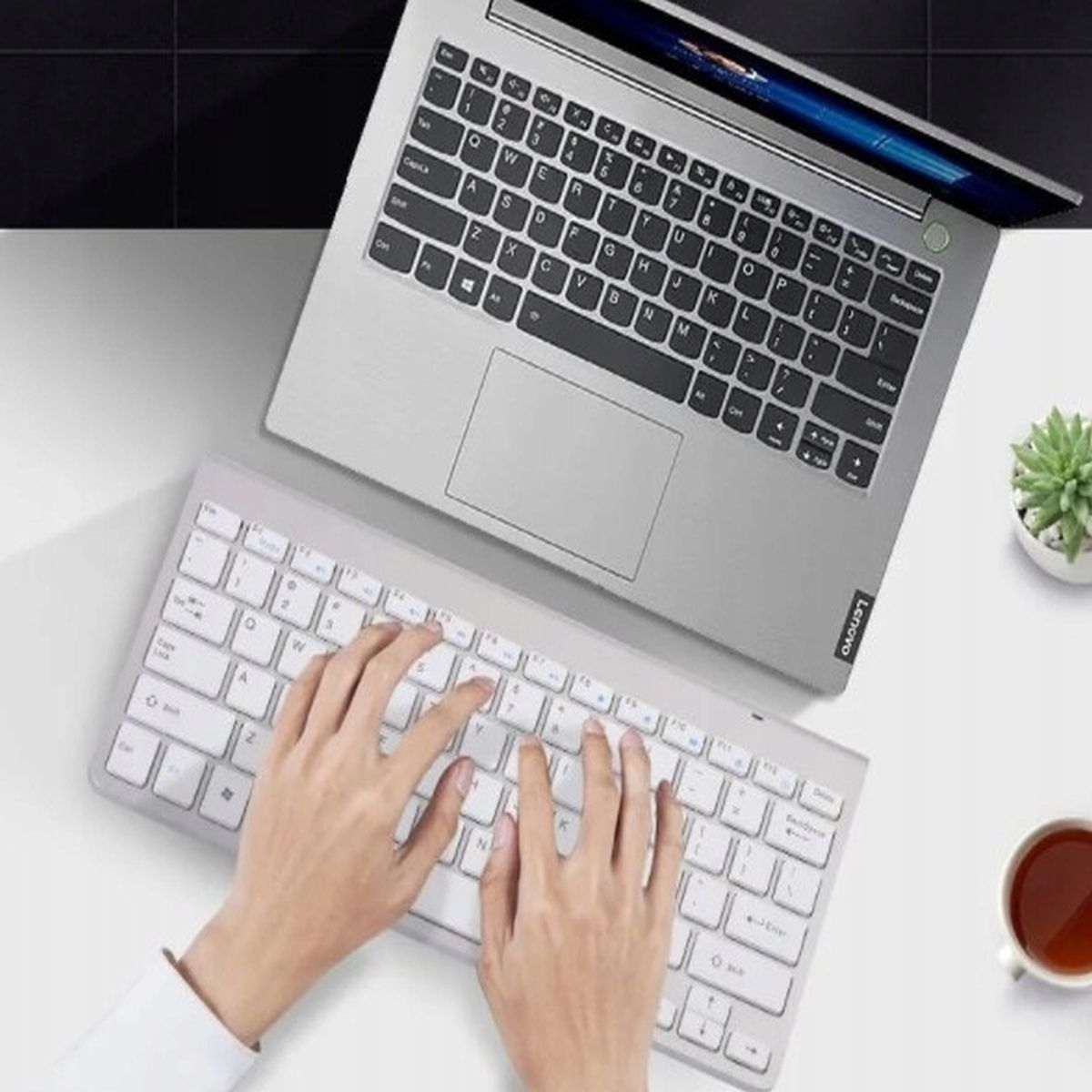 Laptop z białą klawiaturą i rękami piszącymi, obok białej klawiatury.