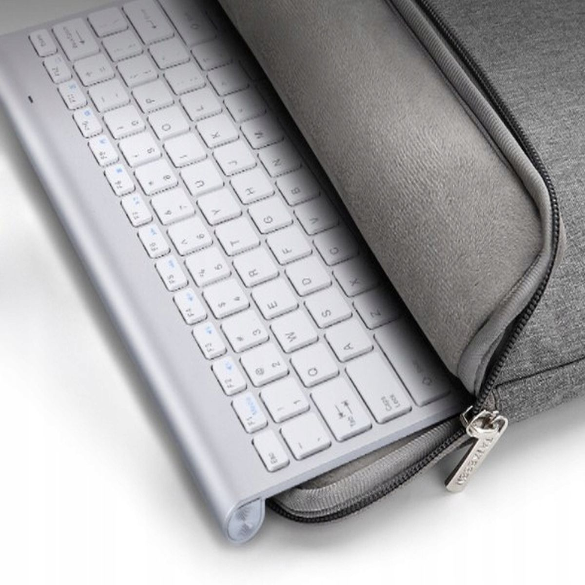 Srebrna klawiatura w szarej obudowie z zamkiem błyskawicznym. Klawiatura ma białe klawisze.