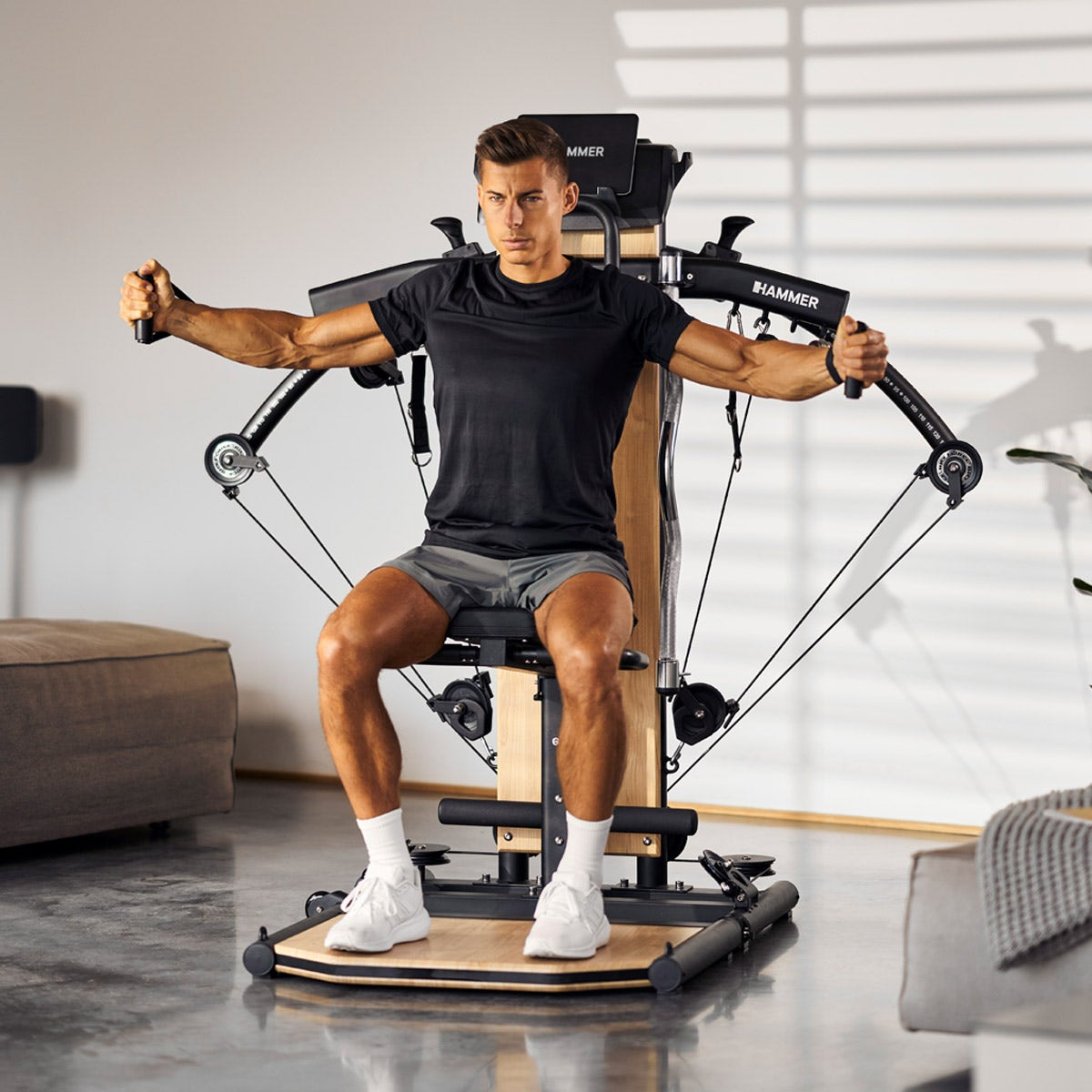 Mann trainiert an einer schwarzen und hölzernen Hammer-Trainingsmaschine. Er zieht an den Armen.