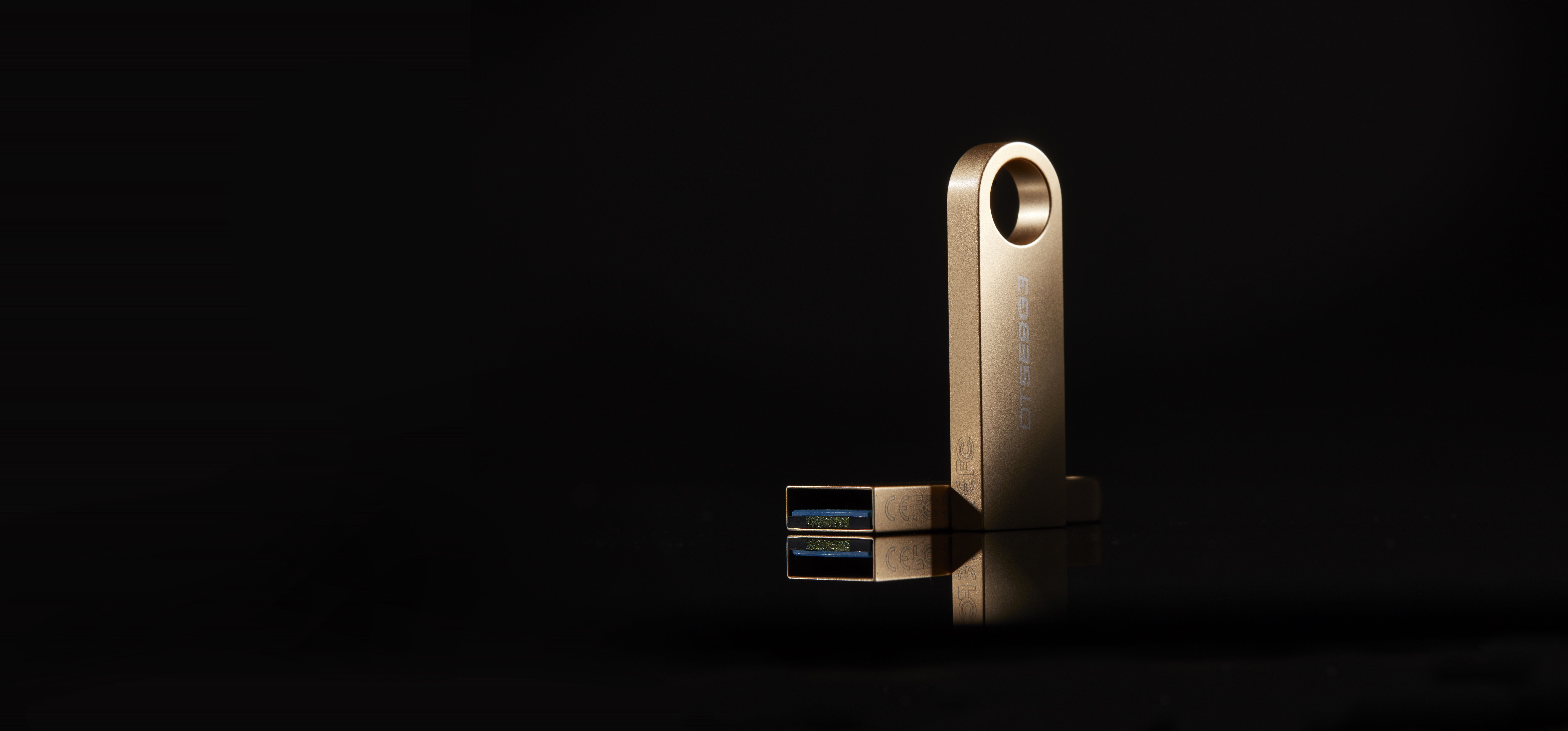 Złoty pendrive USB na czarnym tle, odbijający swój kształt.