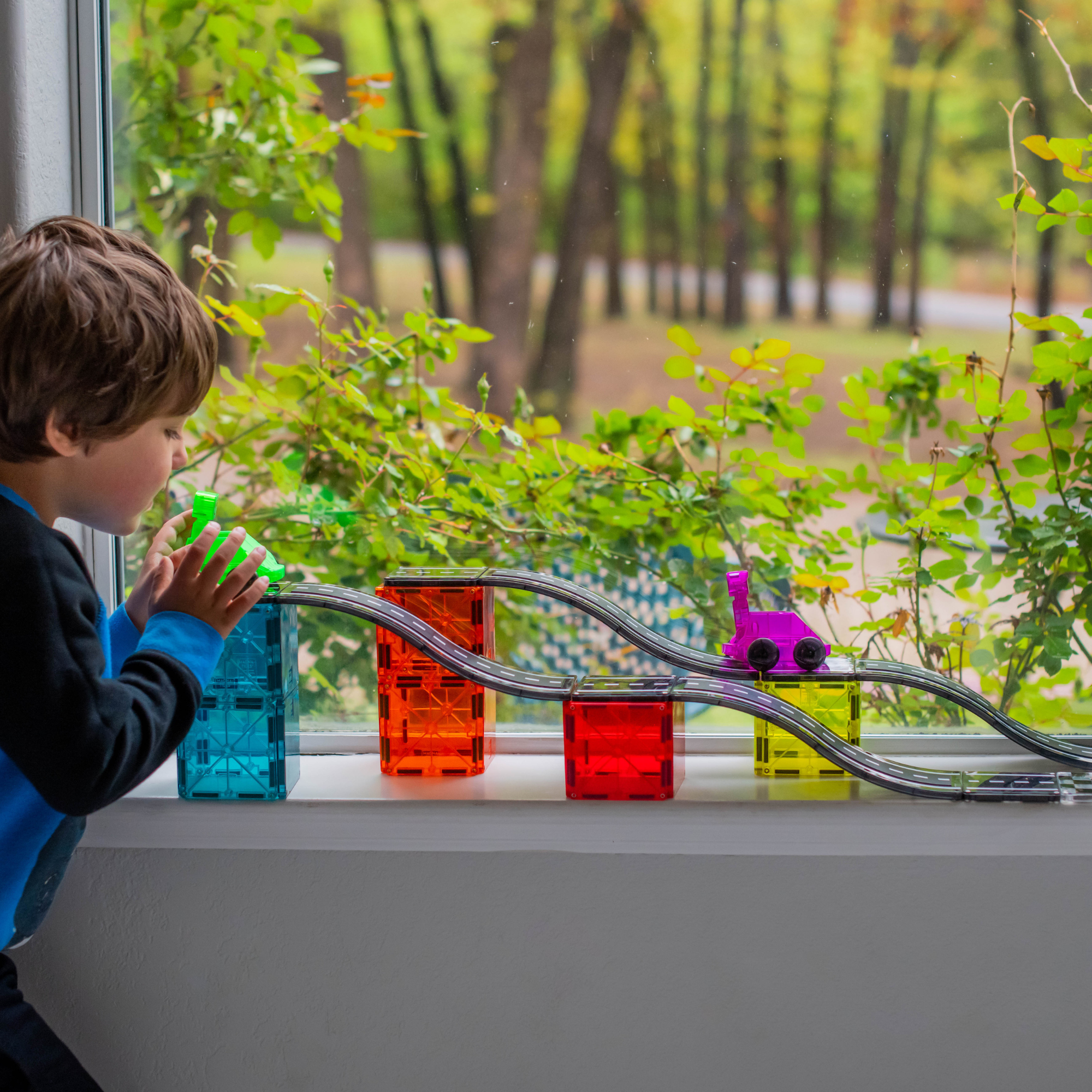 Un enfant jouant avec des blocs de construction colorés et une piste près d'une fenêtre avec des arbres à l'extérieur.