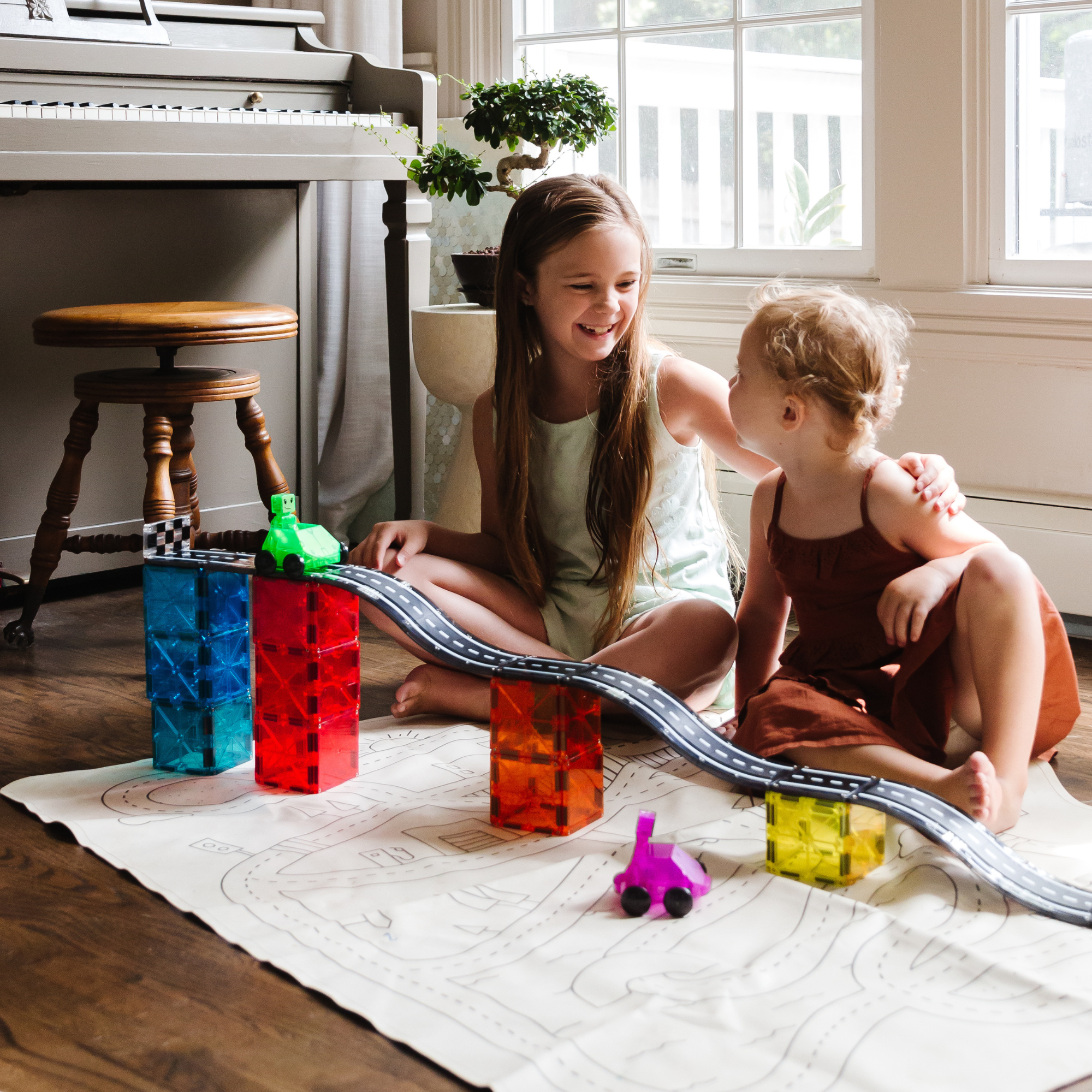 Deux filles jouent avec une piste de jouets colorée, sur une carte, plancher en bois, à l'intérieur.