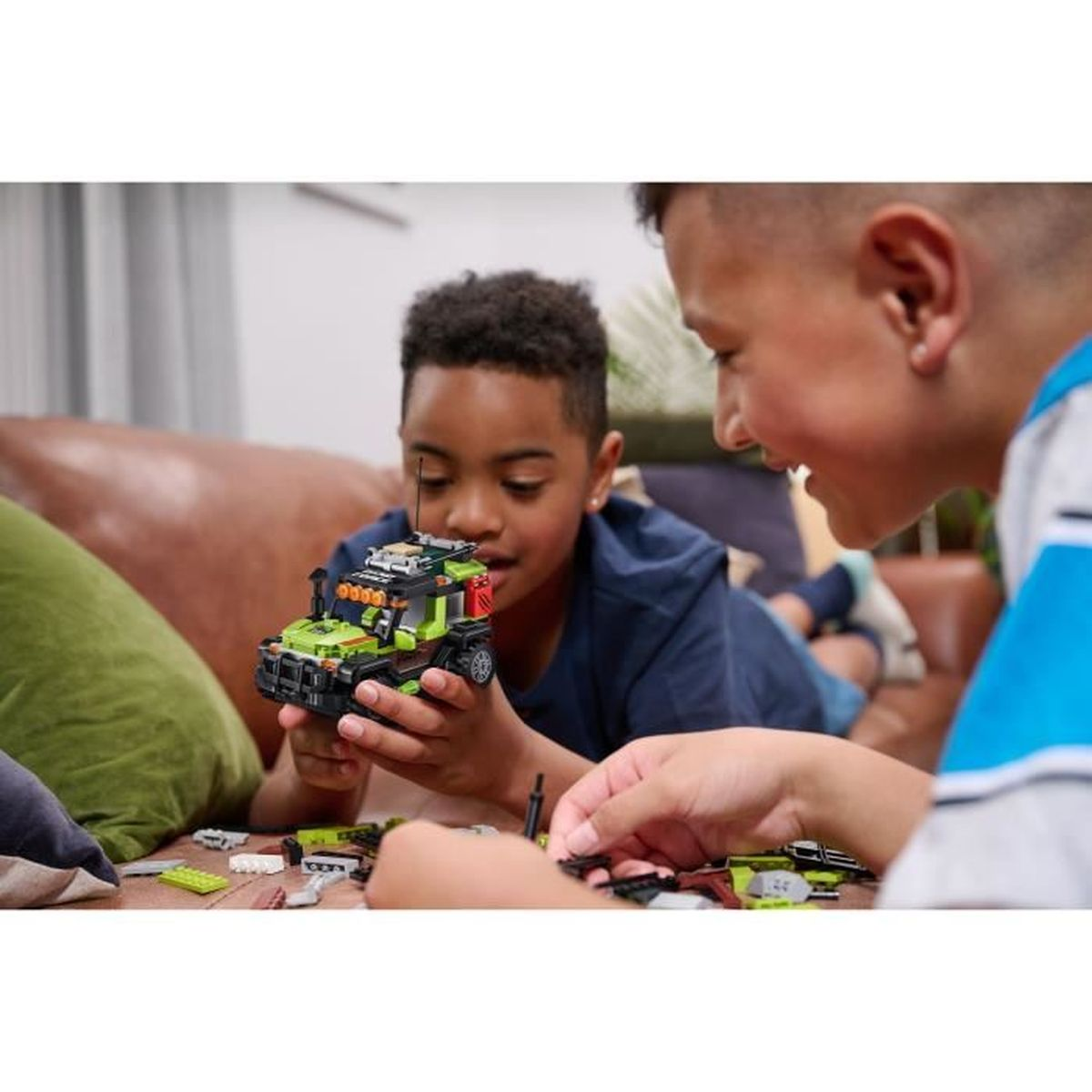 Due ragazzi costruiscono un camion Lego verde e nero. Uno lo tiene, l'altro aggiunge i pezzi.