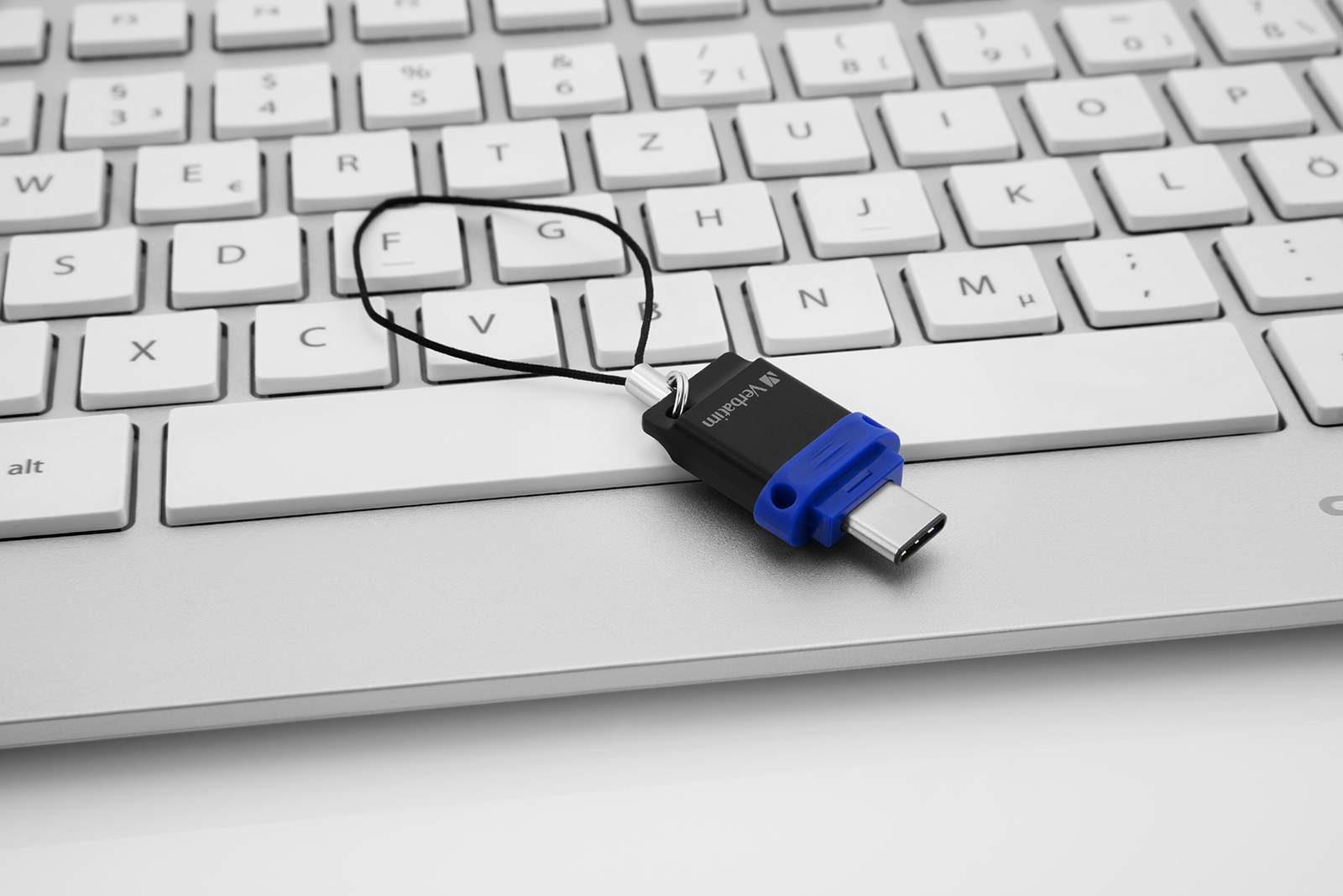 Adapter USB-C podłączony do klawiatury. Jest czarny i niebieski i ma logo Verbatim. Białe tło.