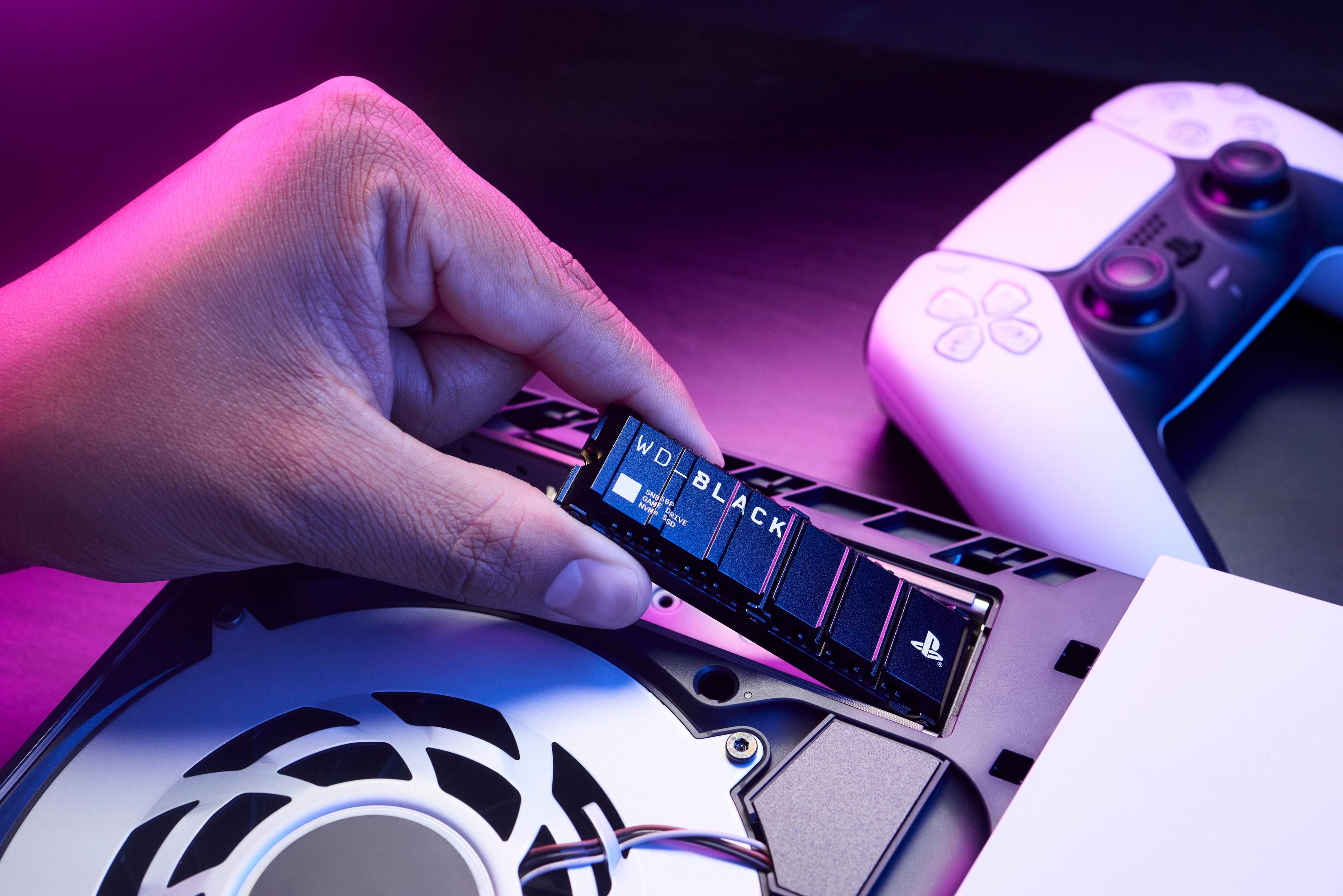 Ręka trzymająca WD Black SSD nad konsolą PS5 z otwartym panelem.
