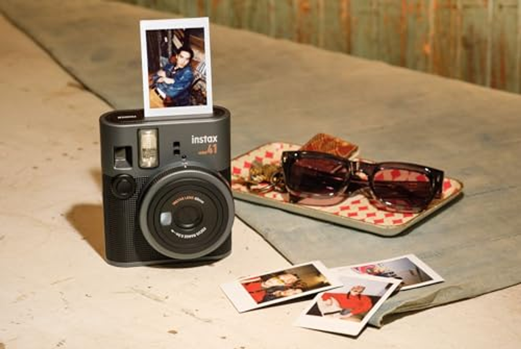 Eine Kamera mit einem Foto und einer Sonnenbrille auf einem Tablett. Andere Fotos liegen auf dem Tisch.
