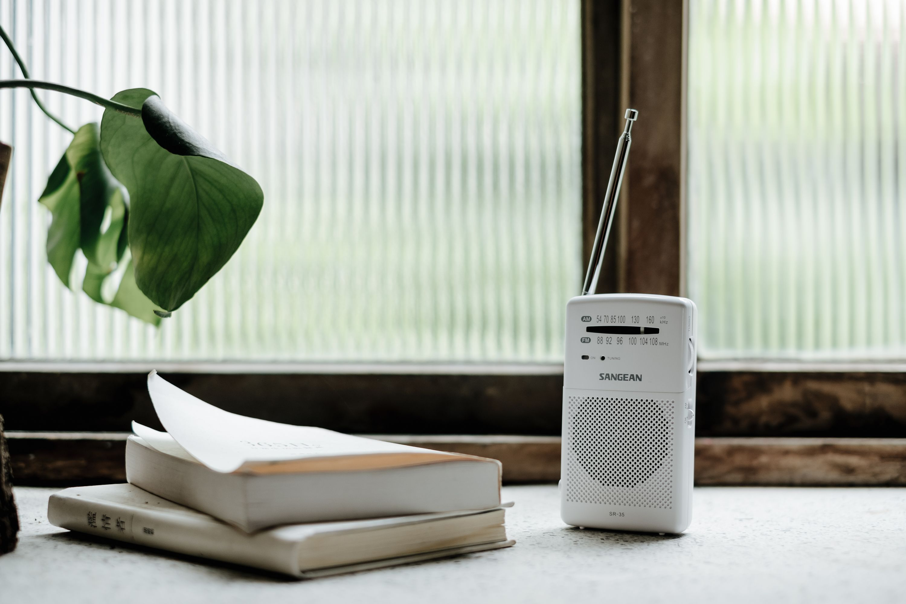 Weißes Radio mit Antenne, Bücher und Blätter an einem Fenster mit unscharfem Hintergrund.