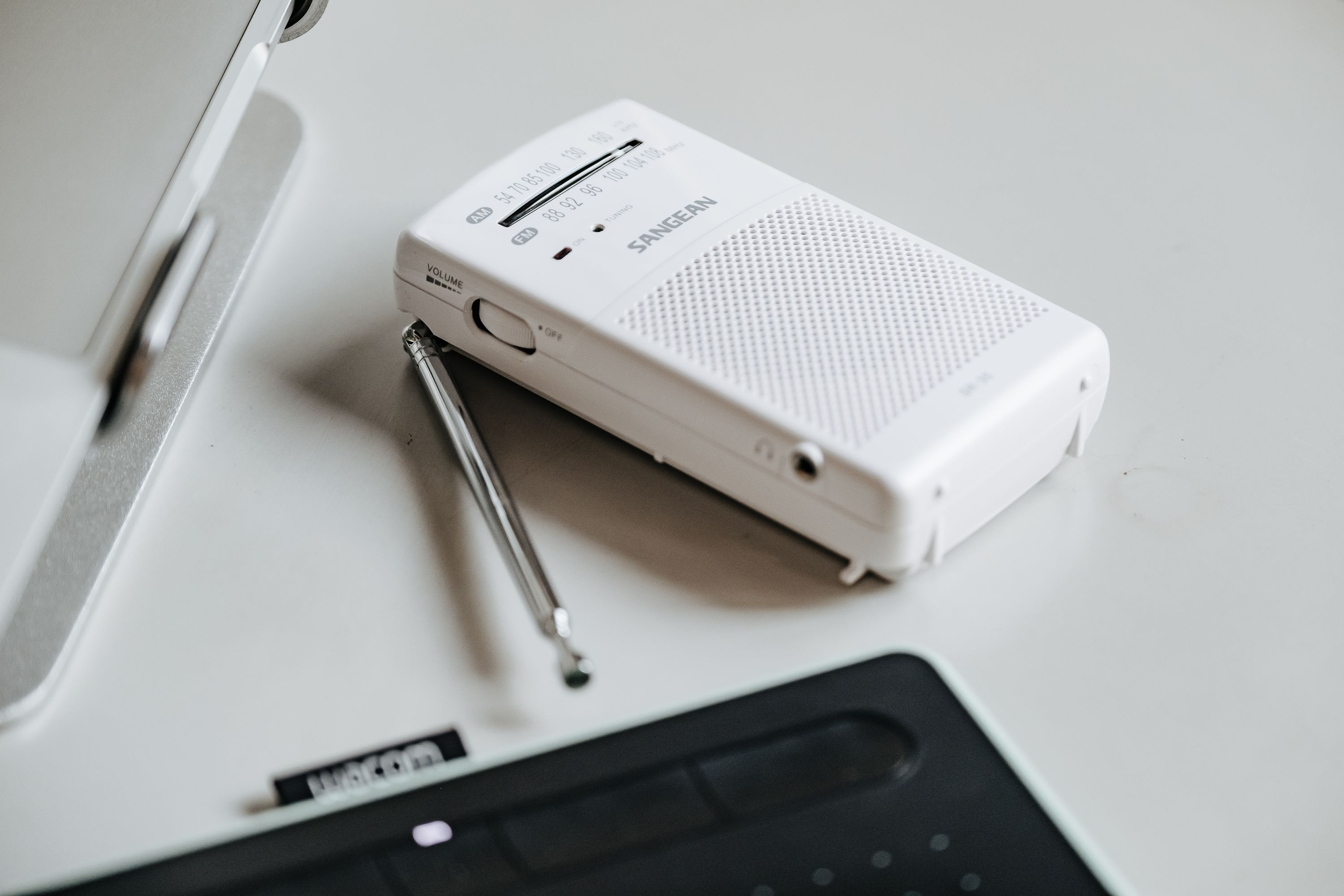 Radio portátil blanco con antena, colocado sobre una superficie blanca, junto a otros objetos.