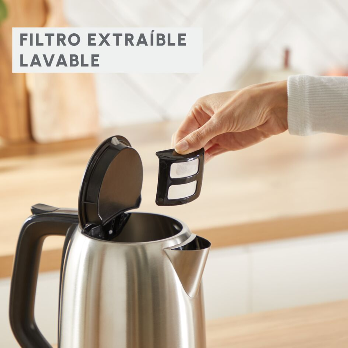 Una mano rimuove un filtro nero da un bollitore elettrico in acciaio inossidabile, con il testo 'FILTRO EXTRAÍBLE LAVABLE'.