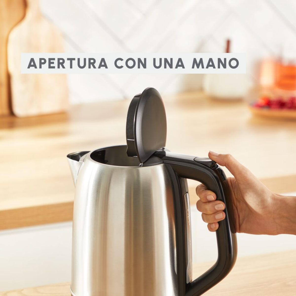 Bollitore in acciaio inox con manico nero, coperchio aperto. Testo: 'APERTURA CON UNA MANO'.