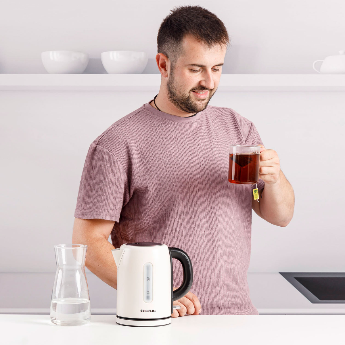 Uomo con tè, in cucina, bollitore e brocca d'acqua sul tavolo.