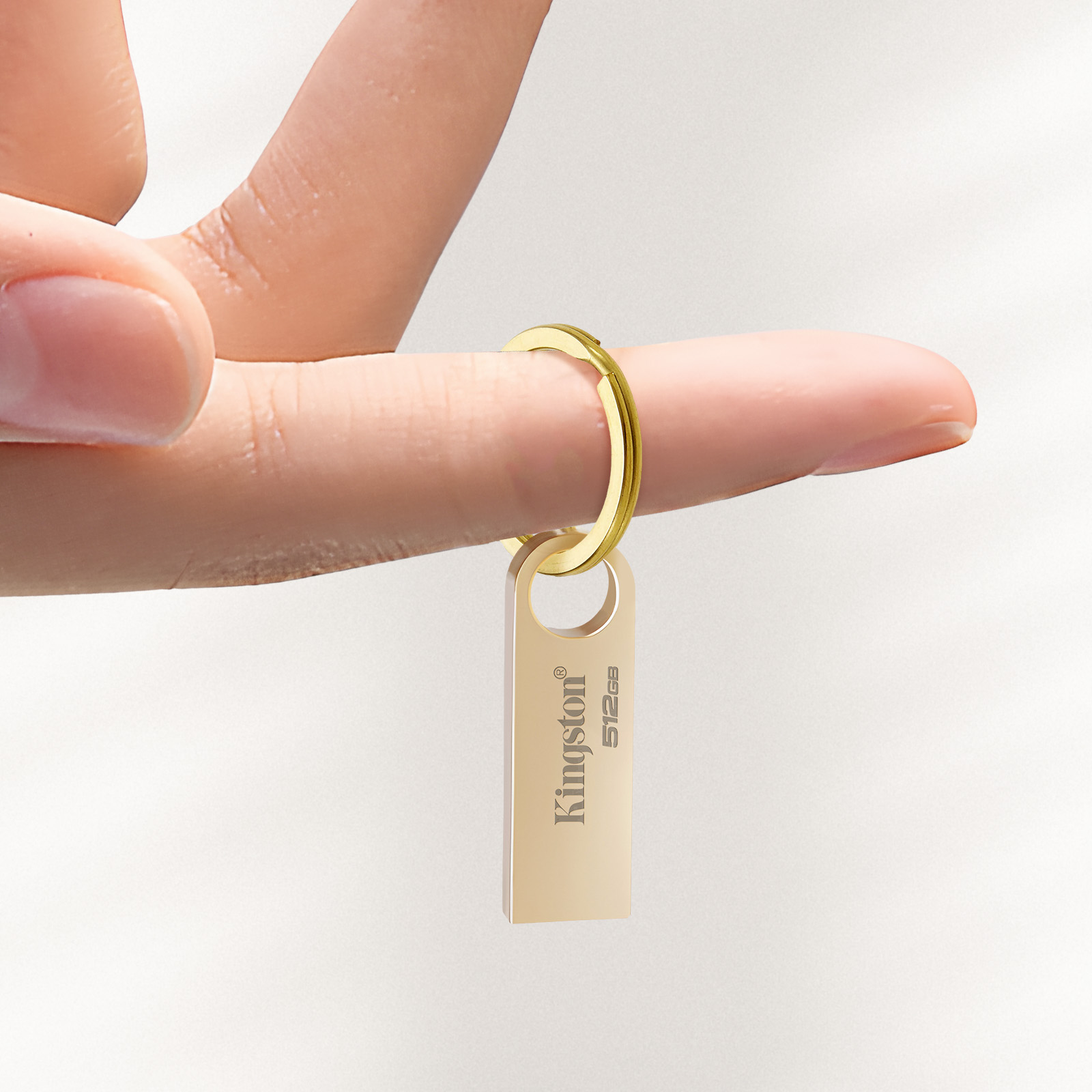 Ręka trzymająca złoty pendrive Kingston. Pendrive jest na złotym kółku i ma logo Kingston.