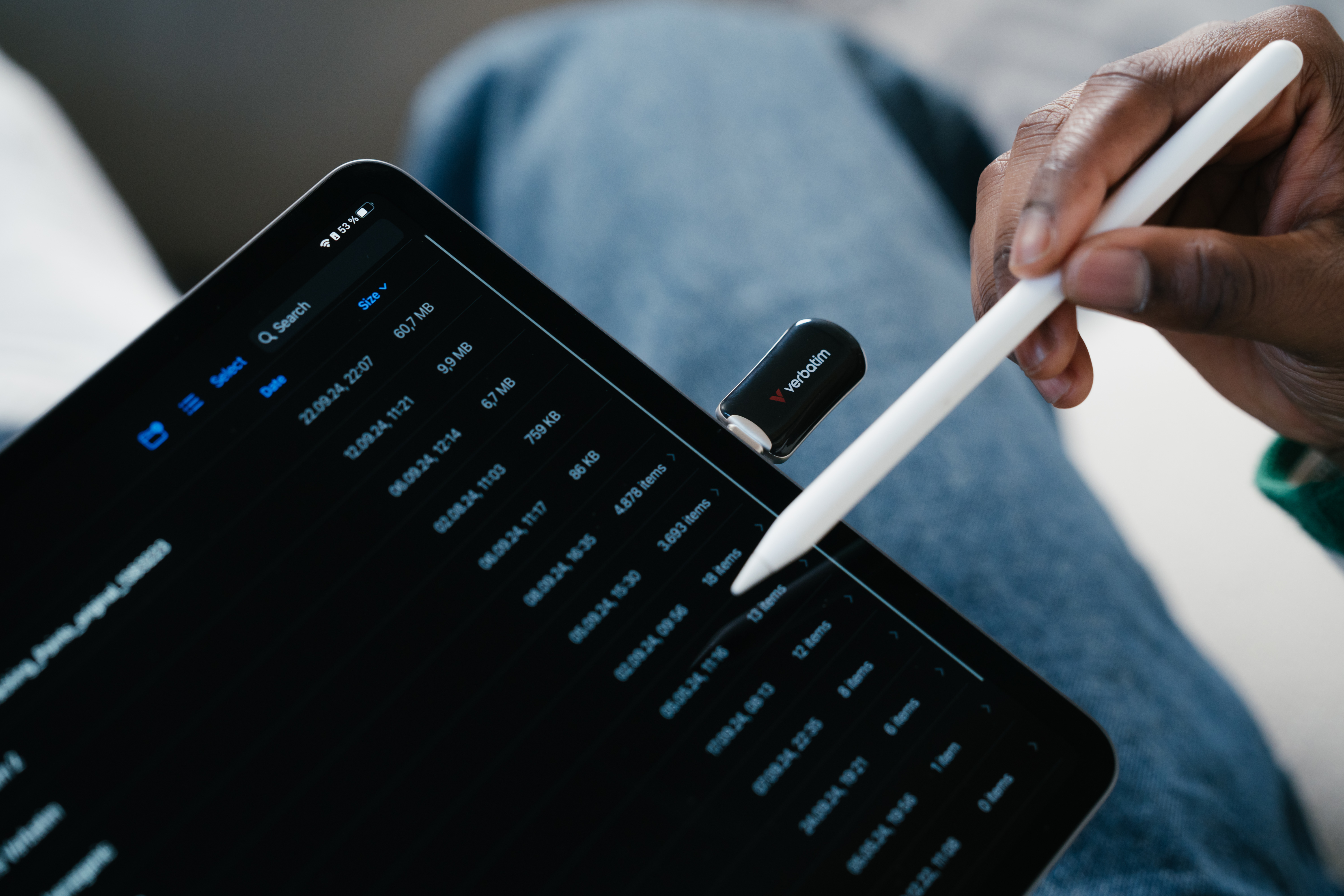 Ręka trzymająca biały rysik w pobliżu czarnego tabletu z plikami i pendrivem.