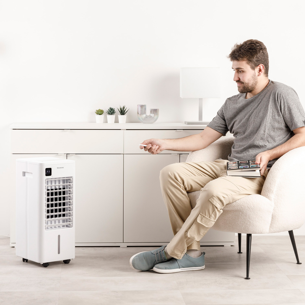 Un hombre sentado, con mando. En su izquierda, un enfriador de aire blanco. Fondo: mueble.
